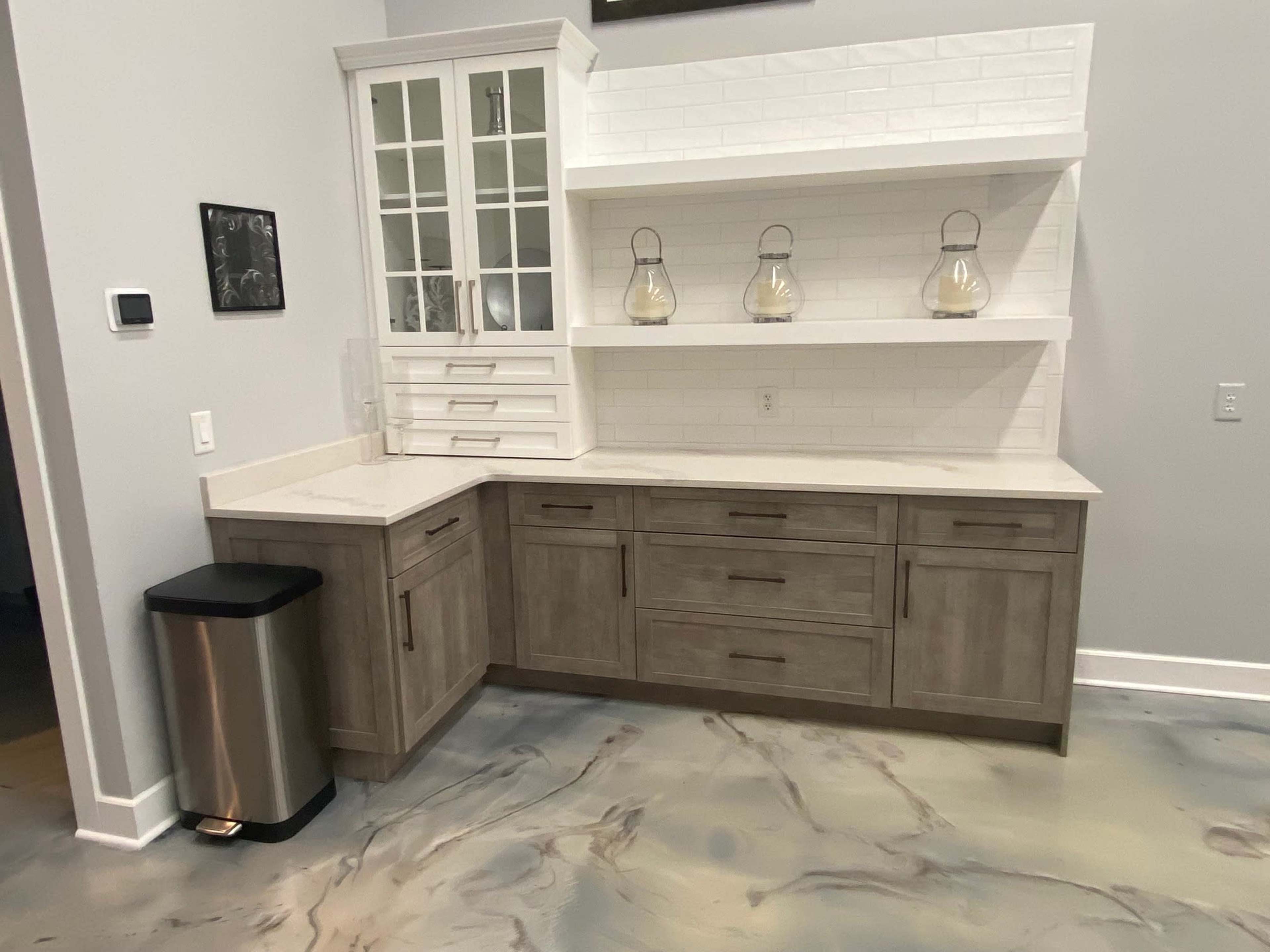 A modern kitchen corner featuring a wooden cabinet with glass doors, open shelving, a countertop, and a trash can.