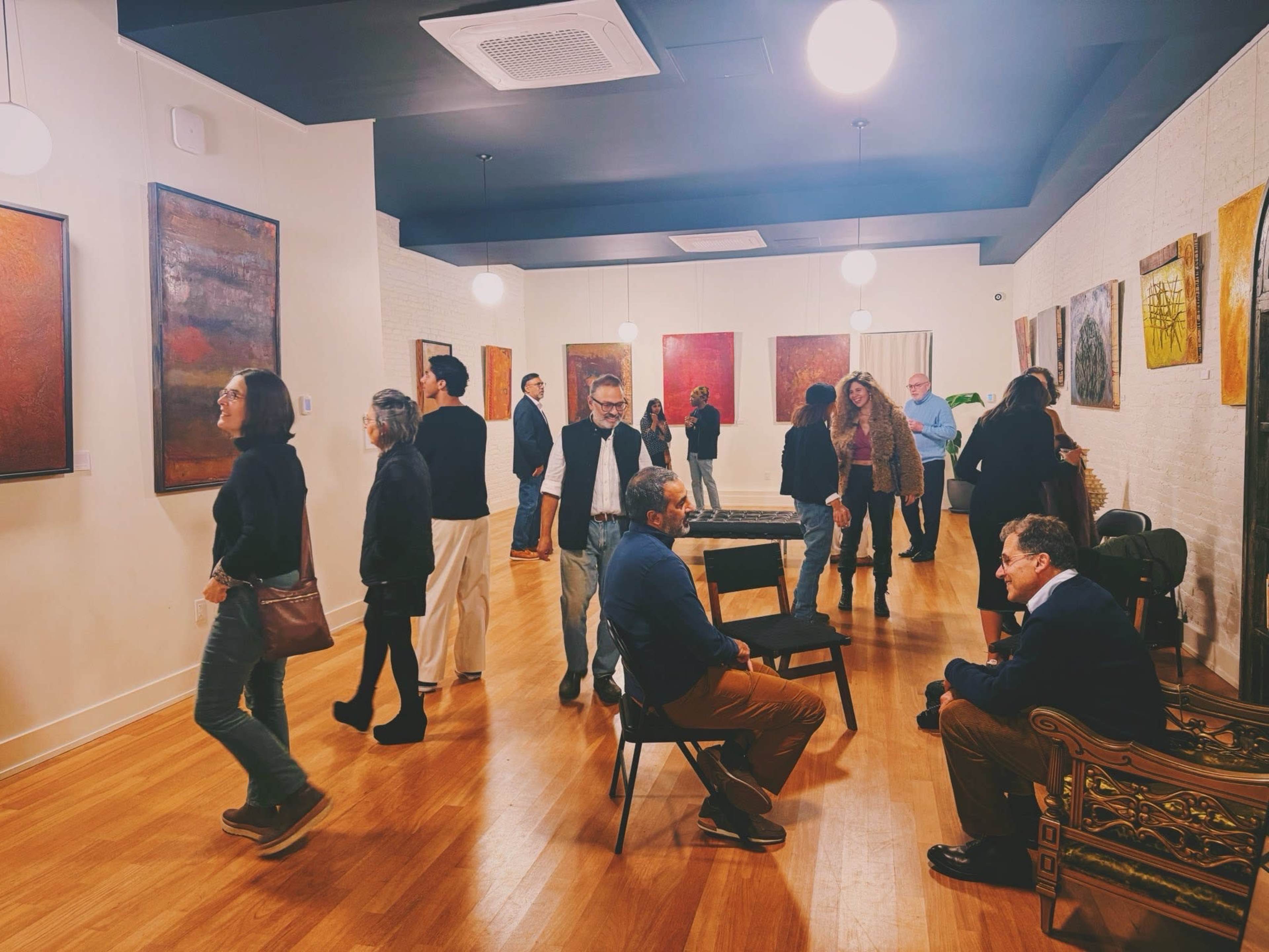 A diverse group of people interacts and views artwork in a well-lit gallery space.