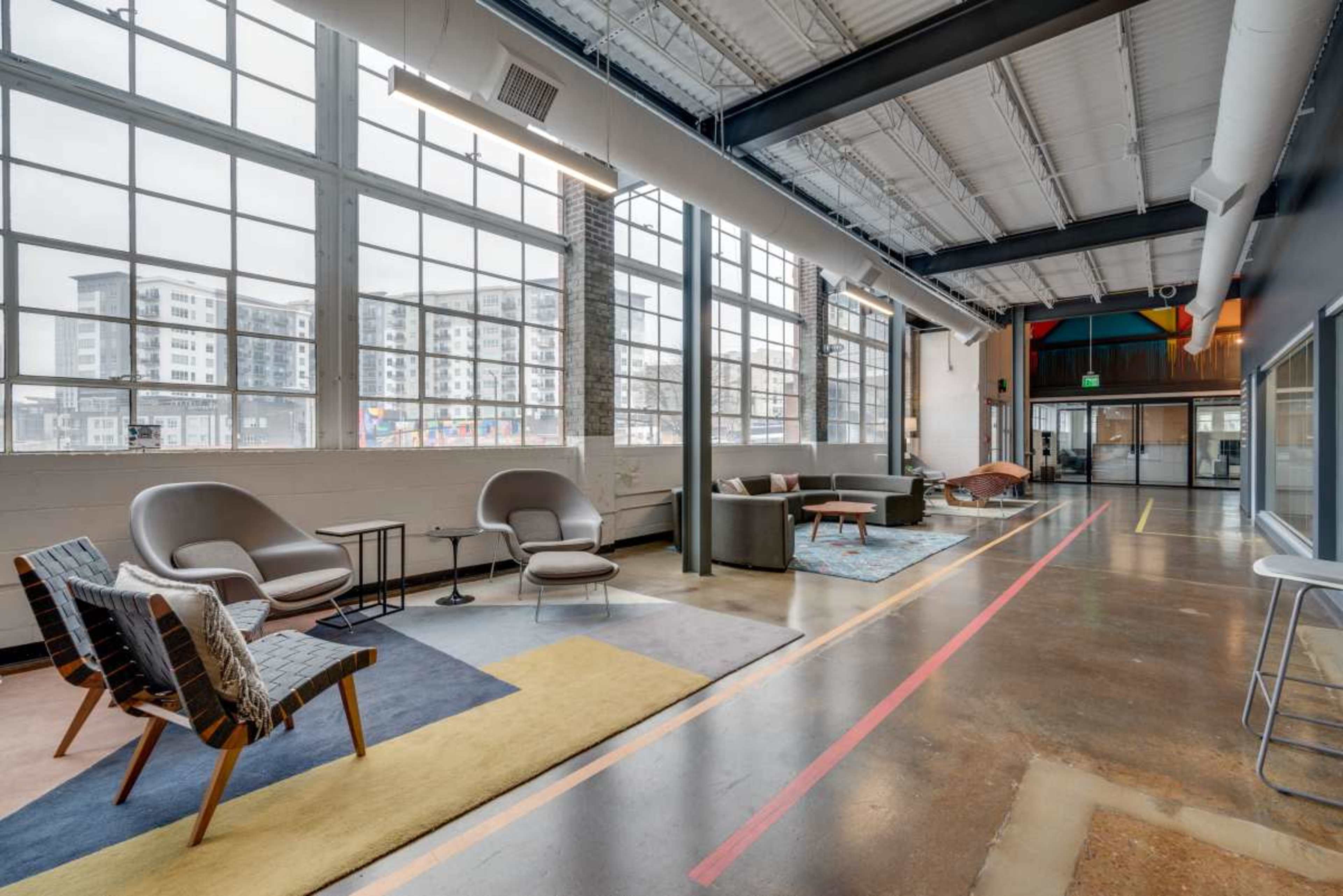 The image shows a spacious, modern lounge area featuring various seating options, large windows, and a polished concrete floor.