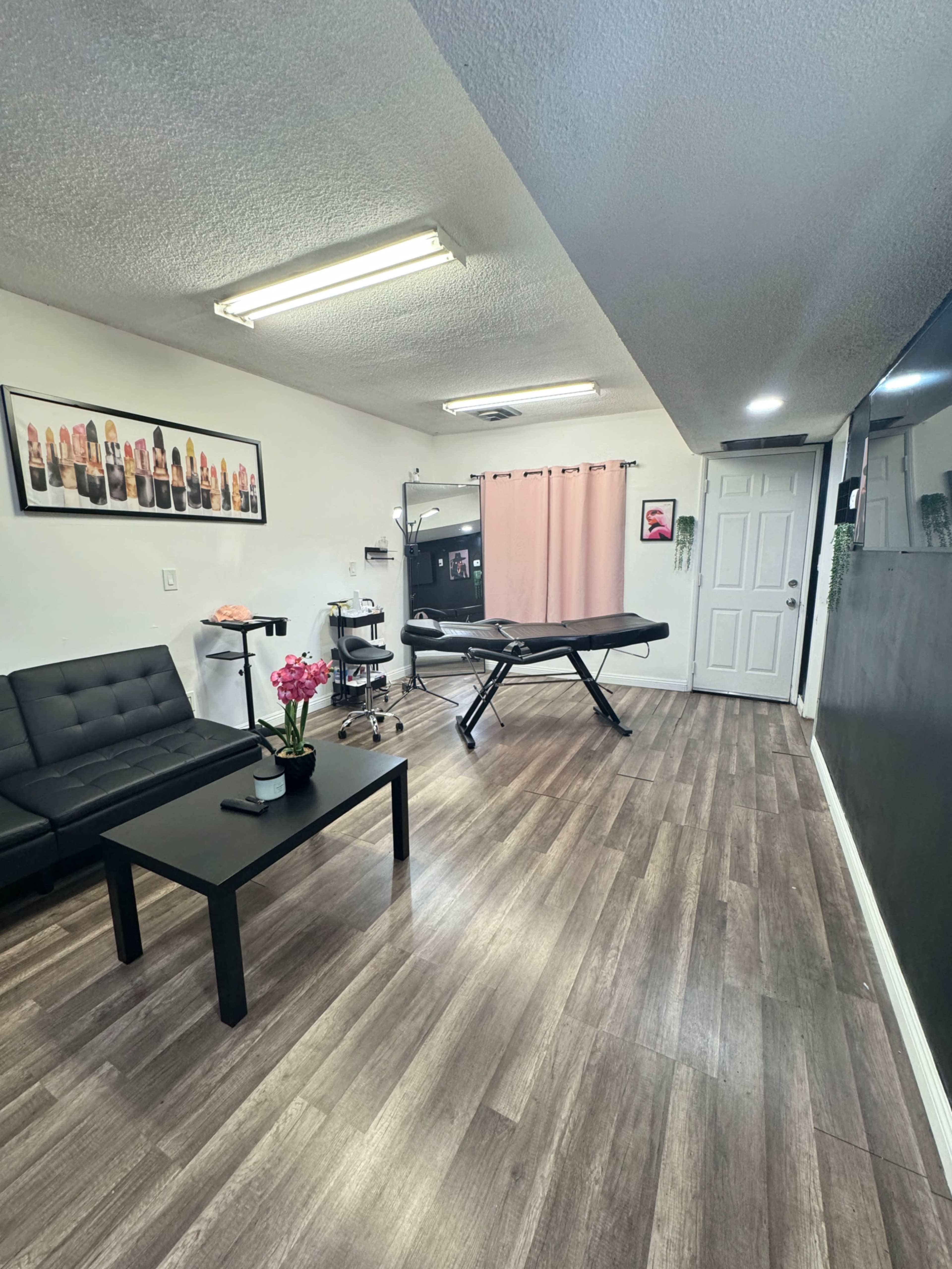 The image shows a small wellness or treatment room with a massage table, a black couch, a coffee table with flowers, and soft lighting.