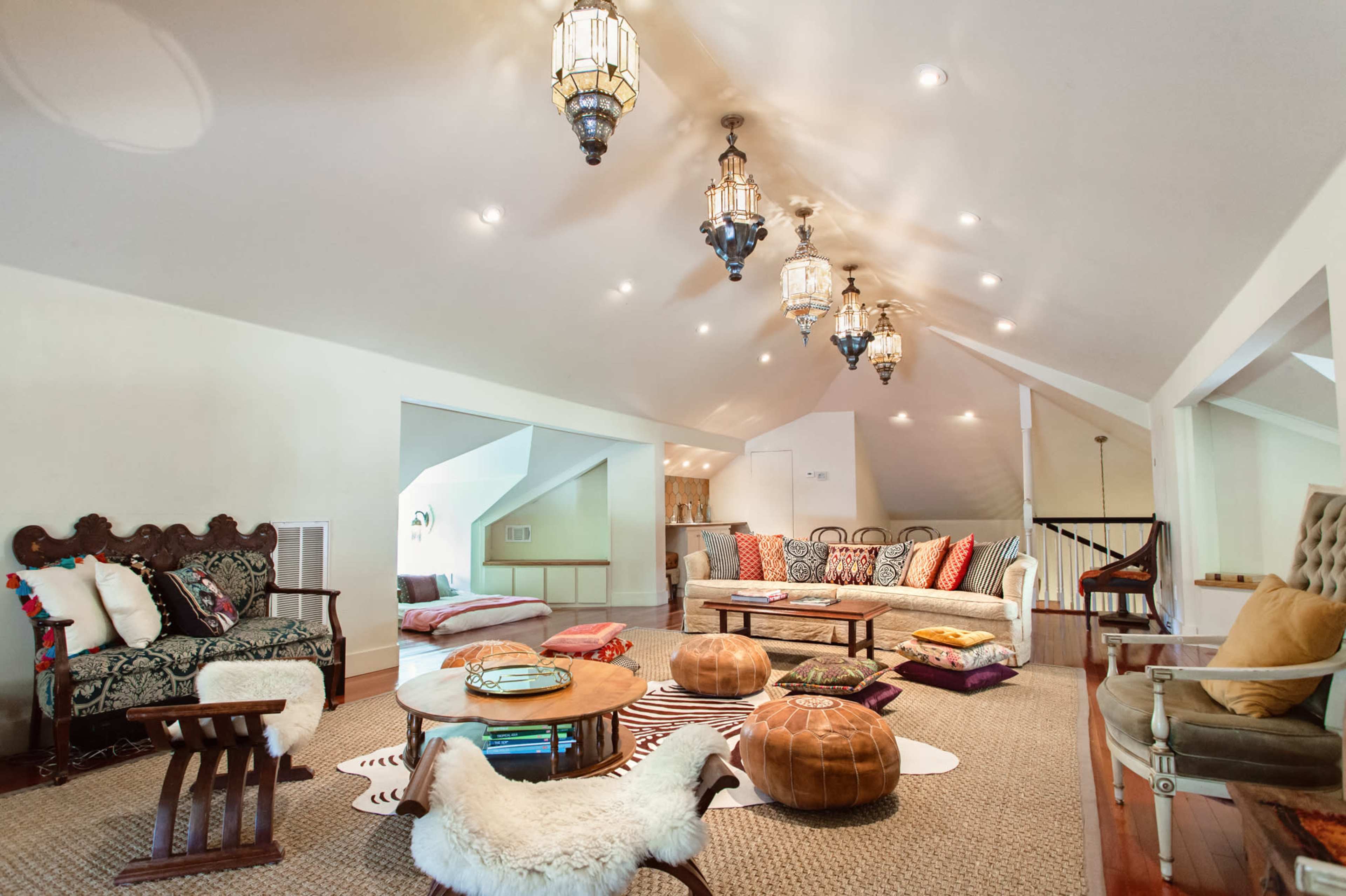 A spacious attic living area adorned with various seating options, decorative lanterns, and a mix of poufs and rugs on the wooden floor.
