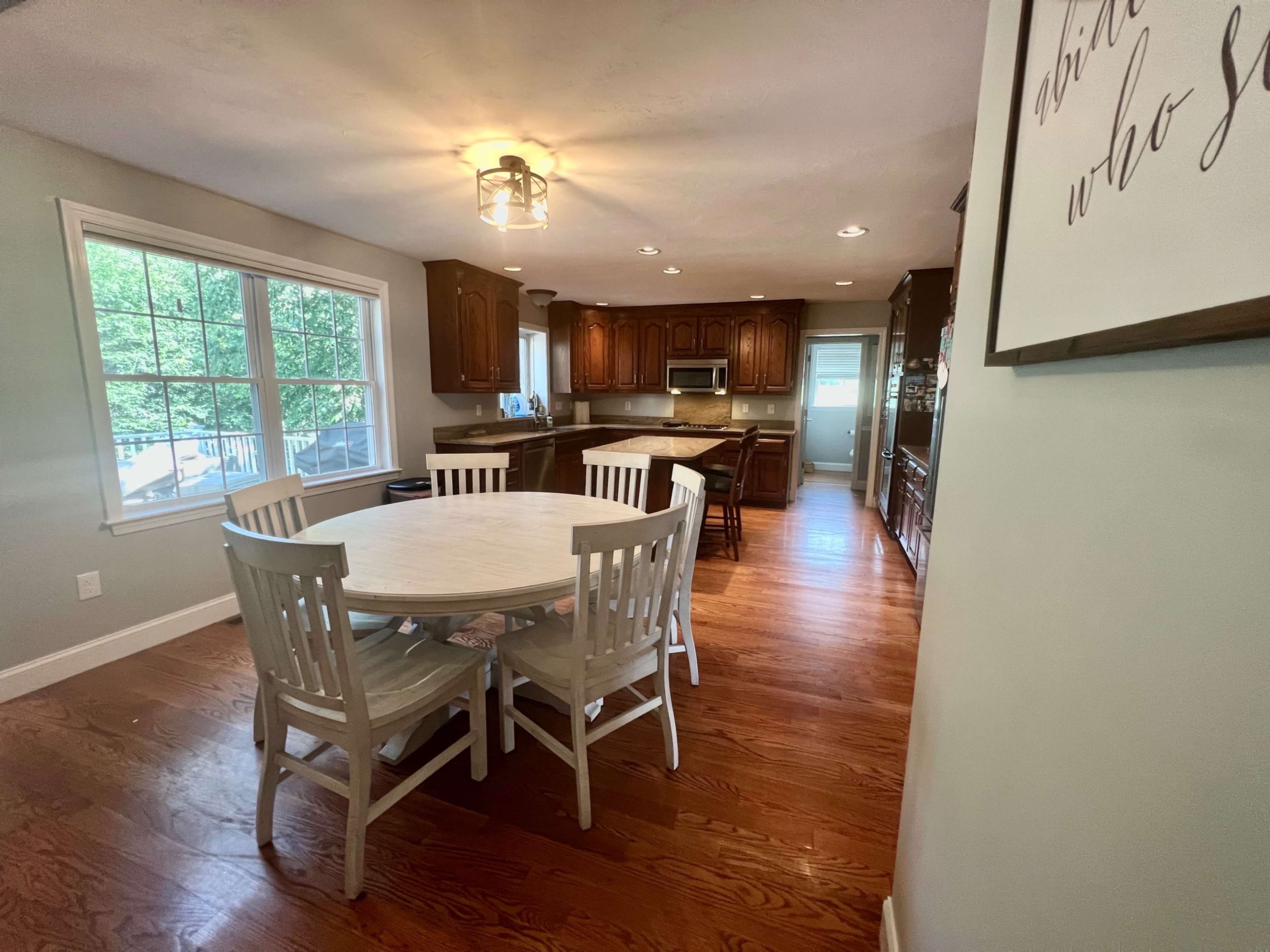 A well-lit kitchen and dining area featuring a circular table with white chairs and wooden cabinets in the background.