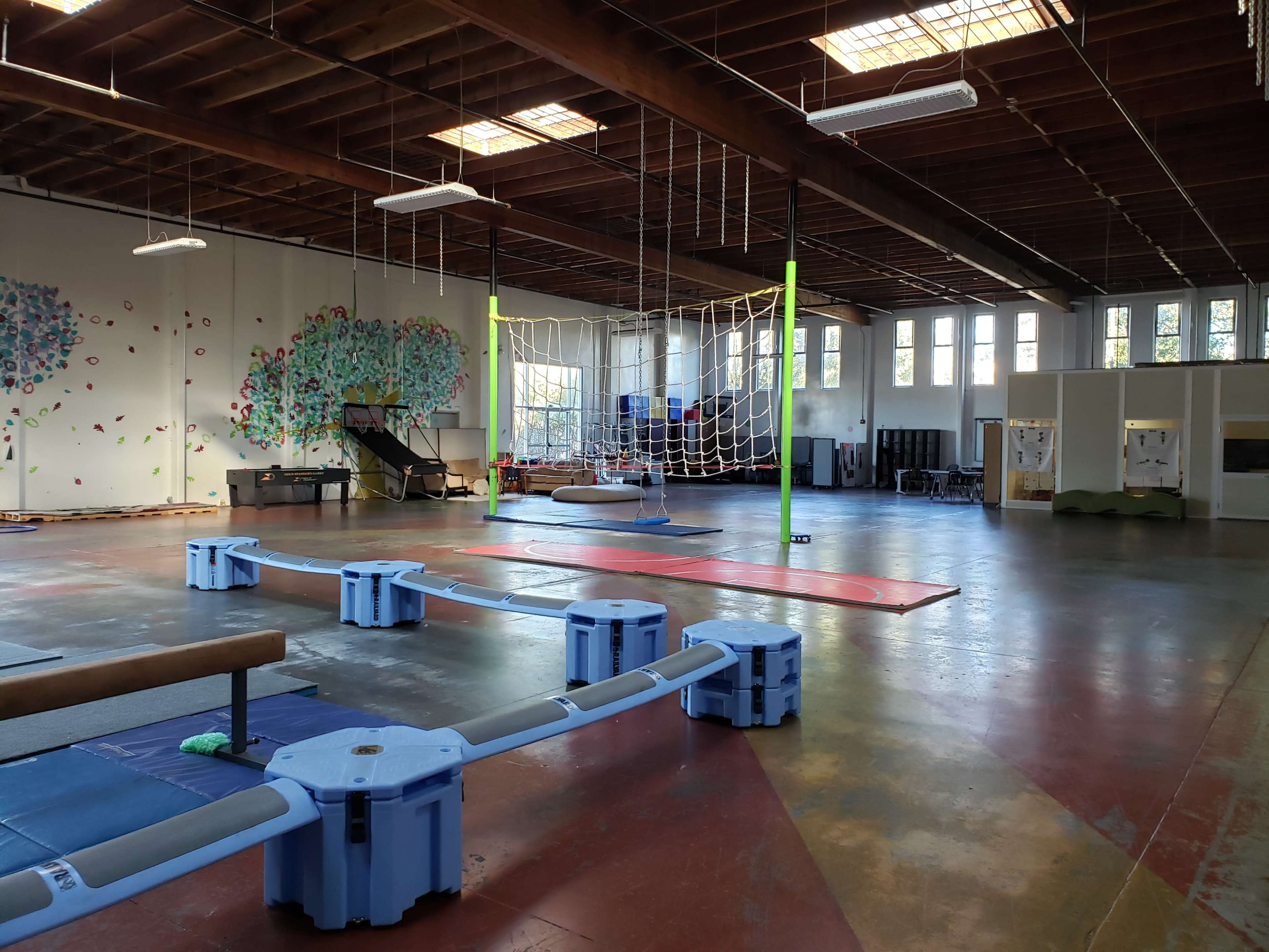 An indoor activity space with climbing structures, mats, and a rope net hanging from the ceiling.