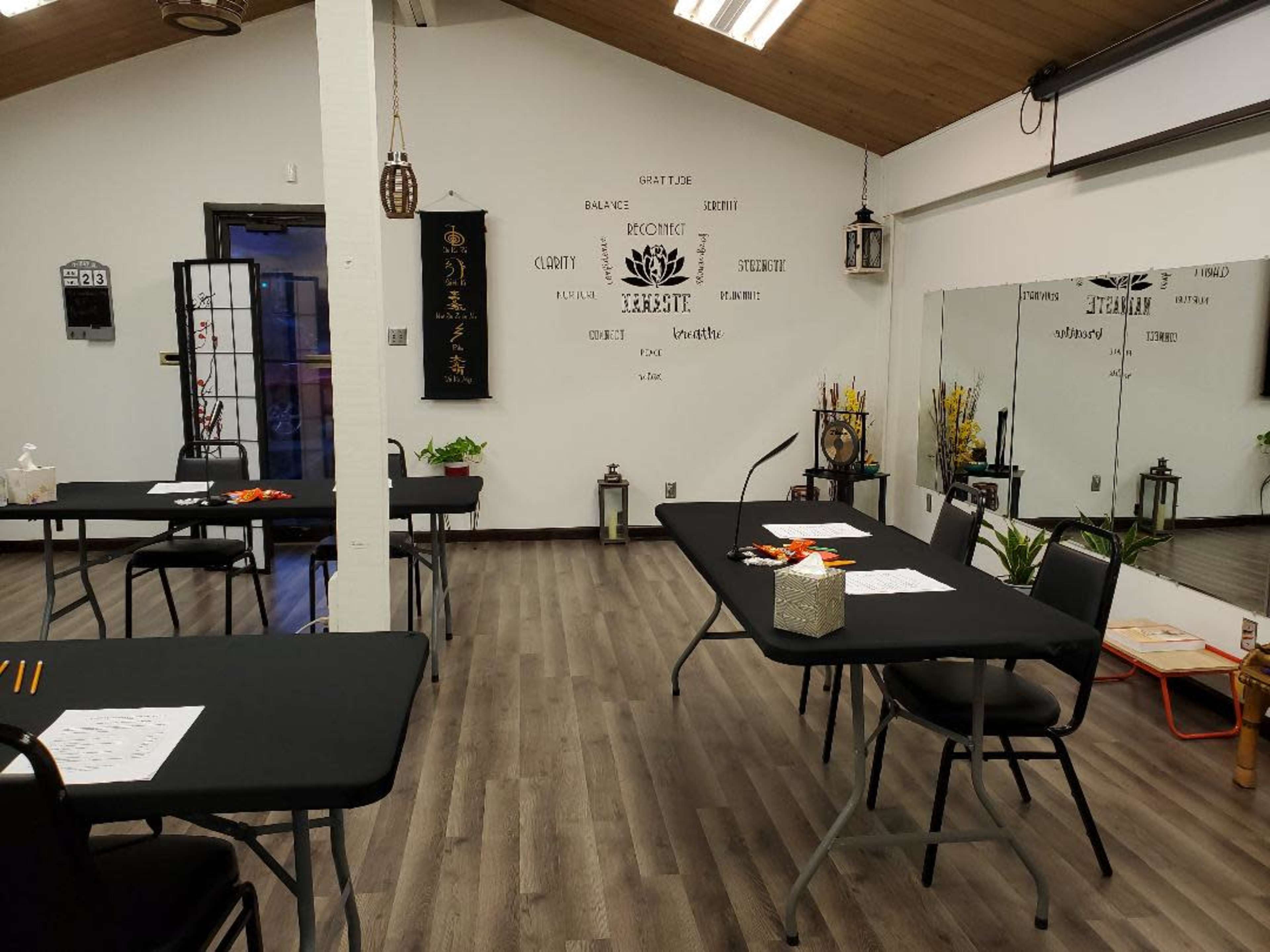 A neatly arranged room with several tables covered in black tablecloths, decorated with plants and lanterns, and featuring a mirror on one wall.