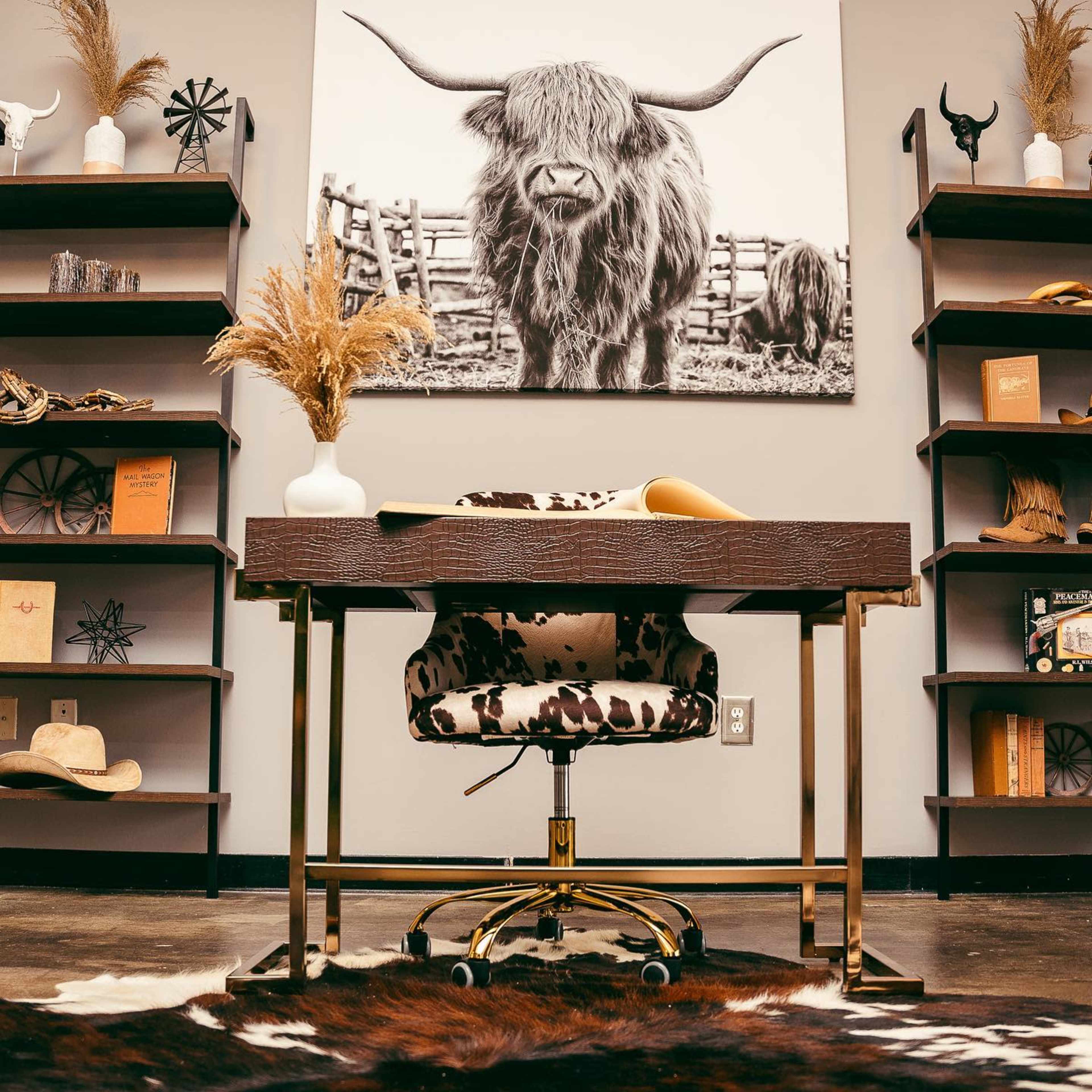A modern office space features a wooden desk with a cowhide chair, surrounded by shelves containing decorative items and a large black-and-white portrait of a Highland cow on the wall.