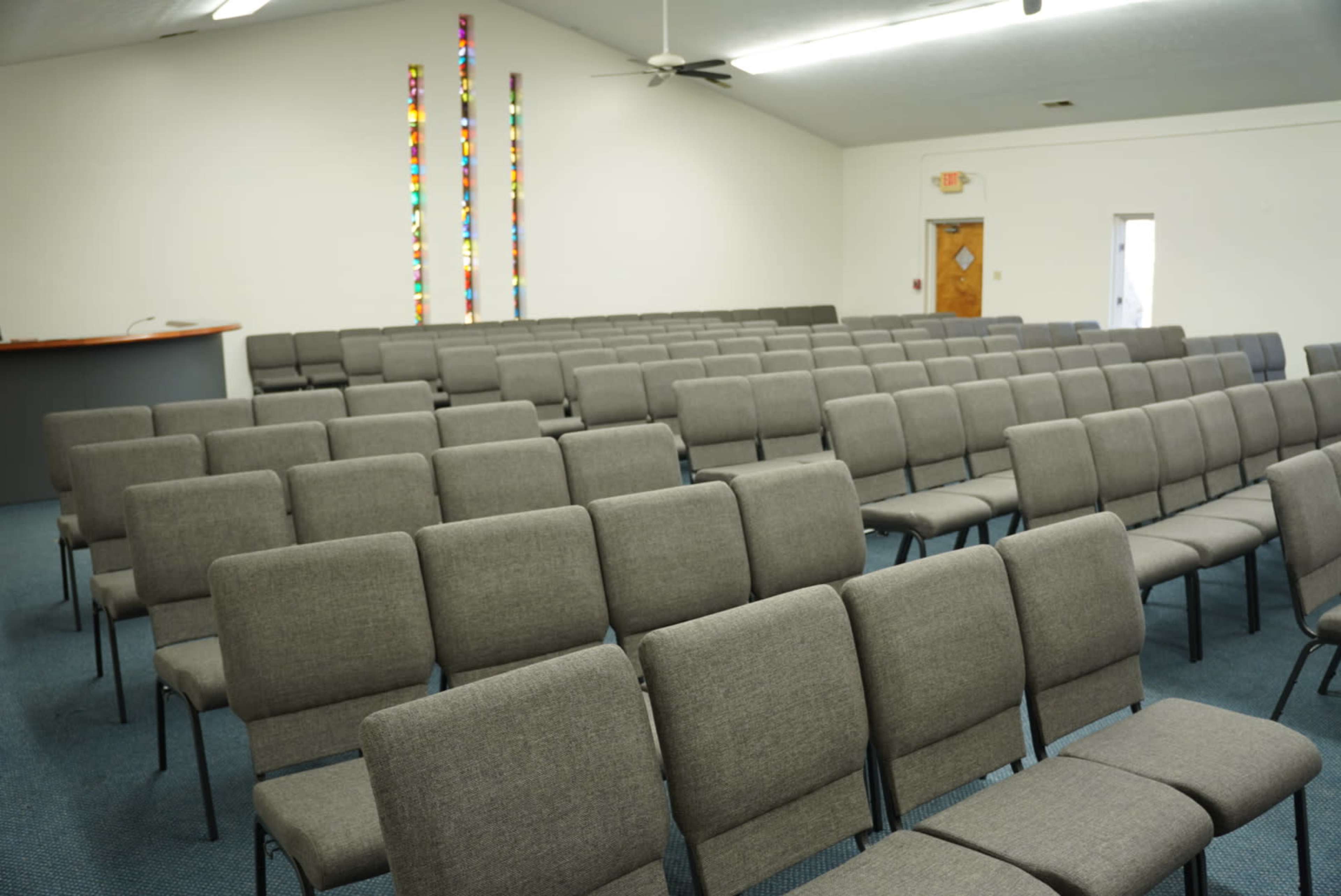 The image shows a room with rows of gray chairs arranged for an assembly, with colorful wall decorations in the background.