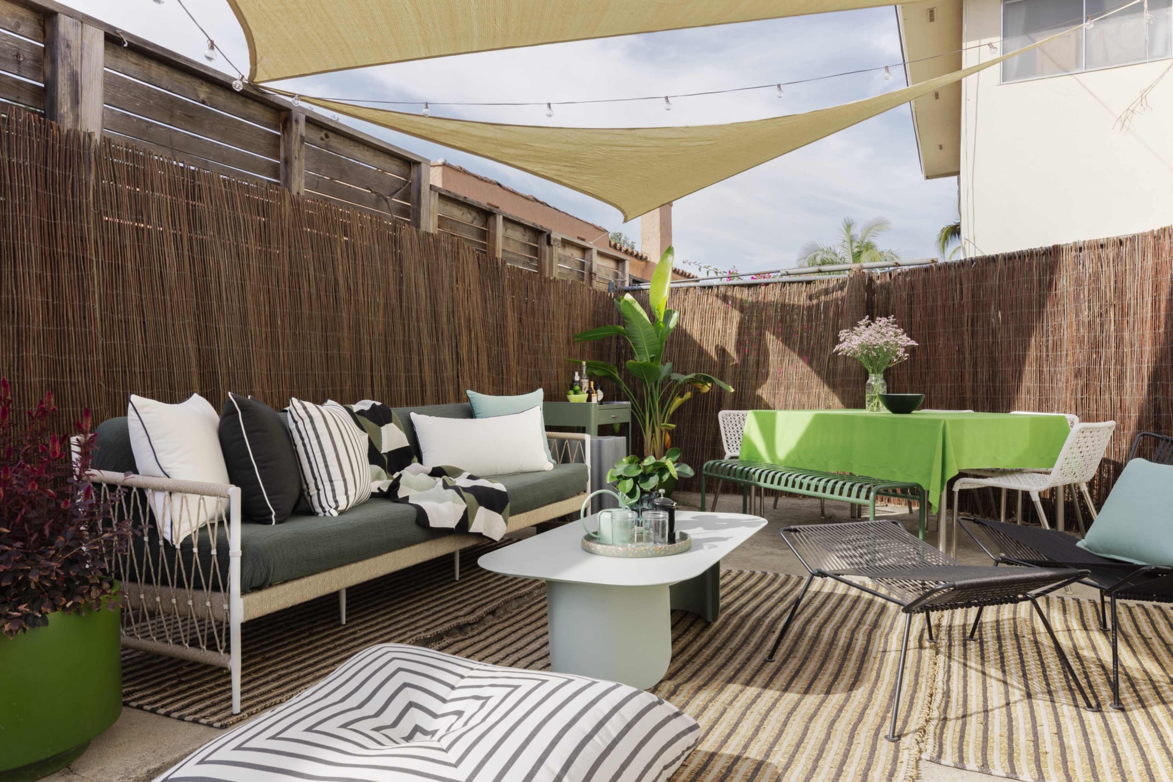 The image shows a stylish outdoor seating area with a mix of green and white furniture, a large sunshade overhead, and decorative plants.
