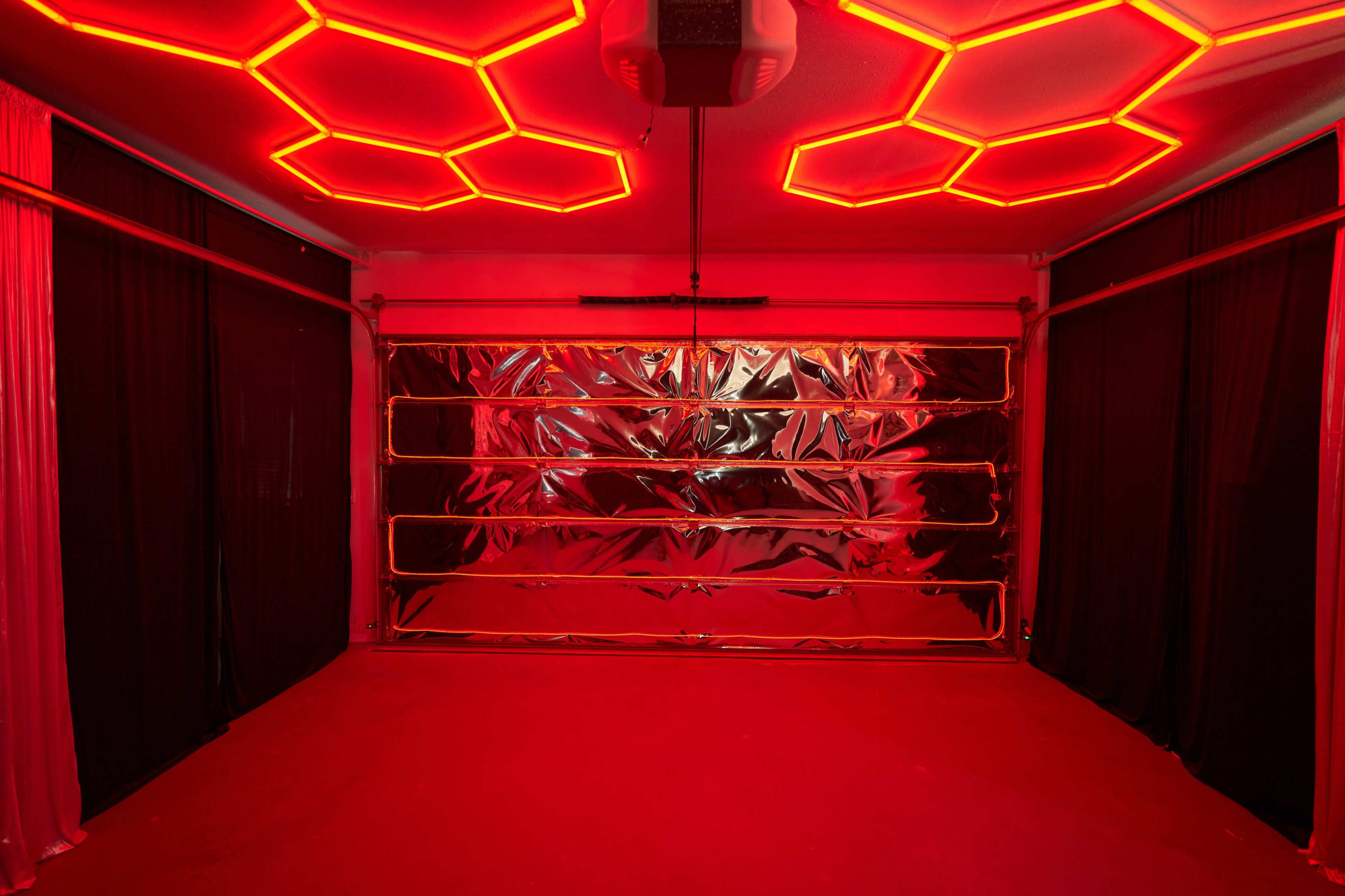 The room features a red-lit ceiling with a honeycomb pattern, black curtains on the sides, and a shiny metallic garage door at the front.
