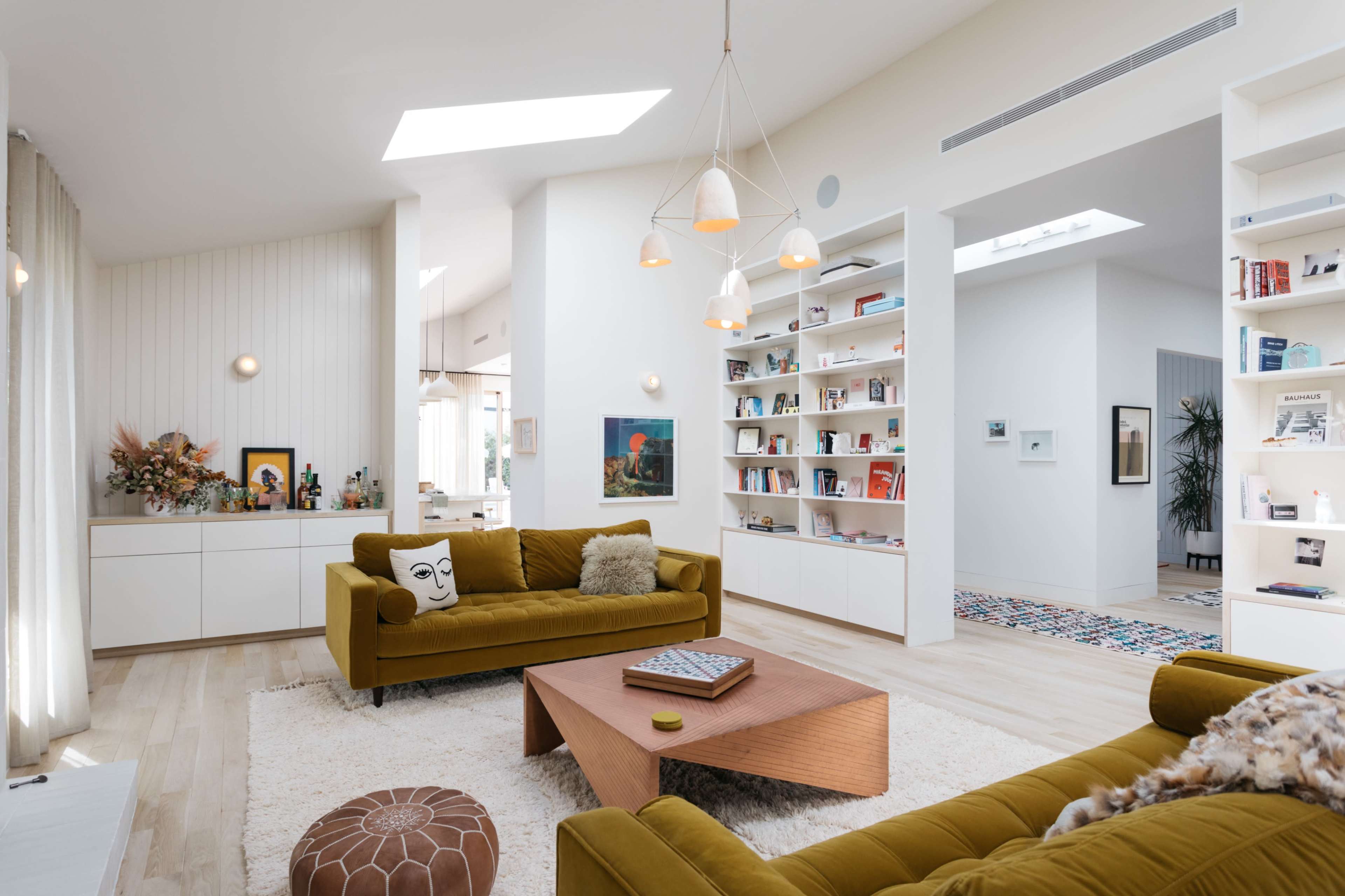 A modern living room features two olive green sofas, a wooden coffee table, and bookshelves filled with various books and decor items.