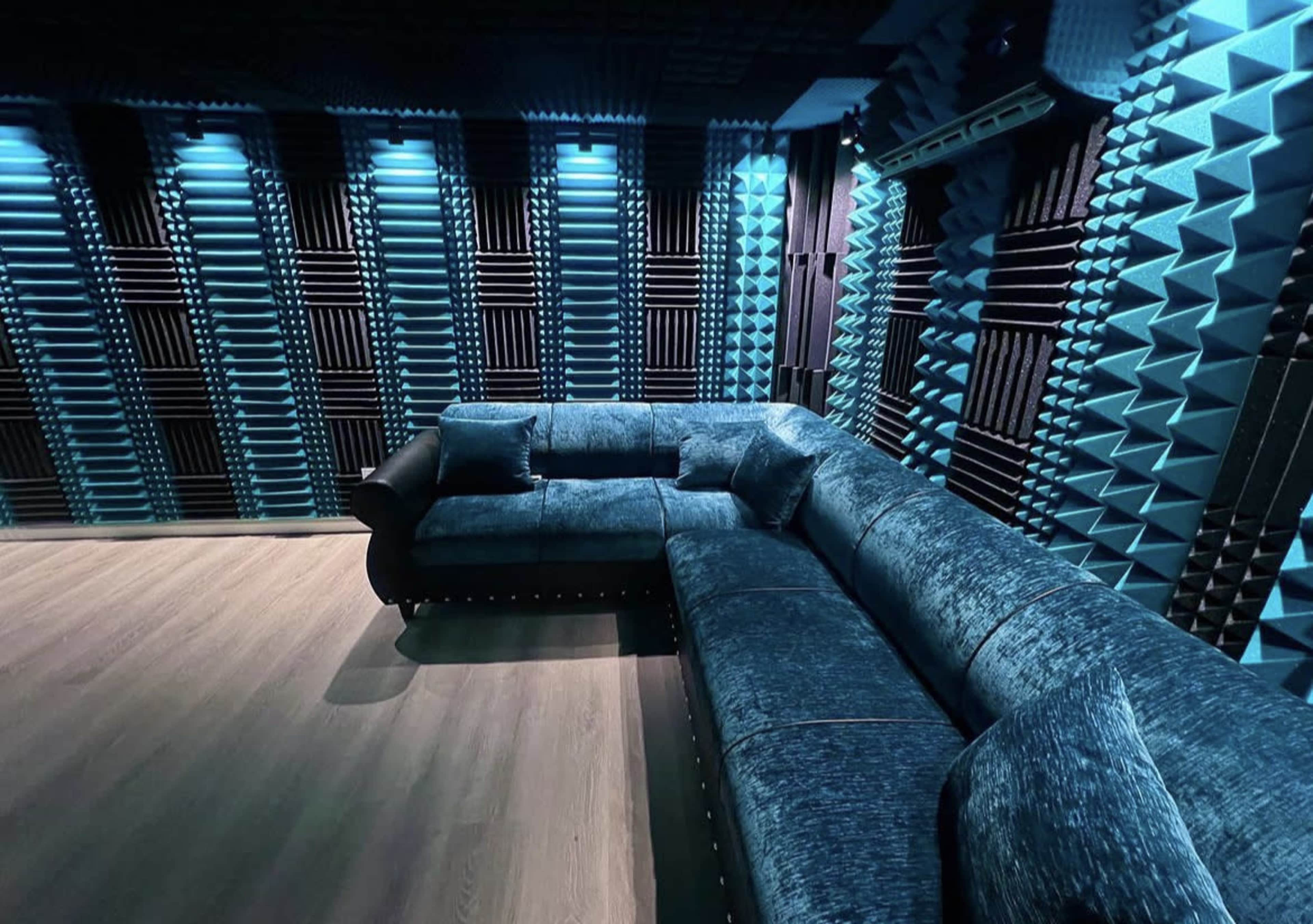 A soundproof room featuring a blue sectional couch and walls covered with acoustic panels.