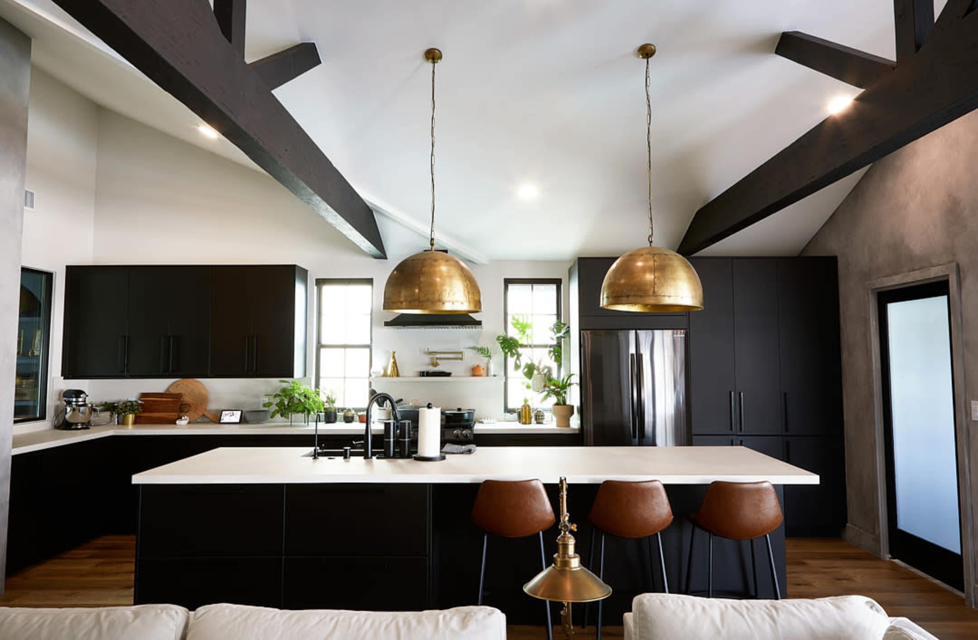 A modern kitchen featuring dark cabinetry, a white countertop, brass pendant lights, and wooden floors.