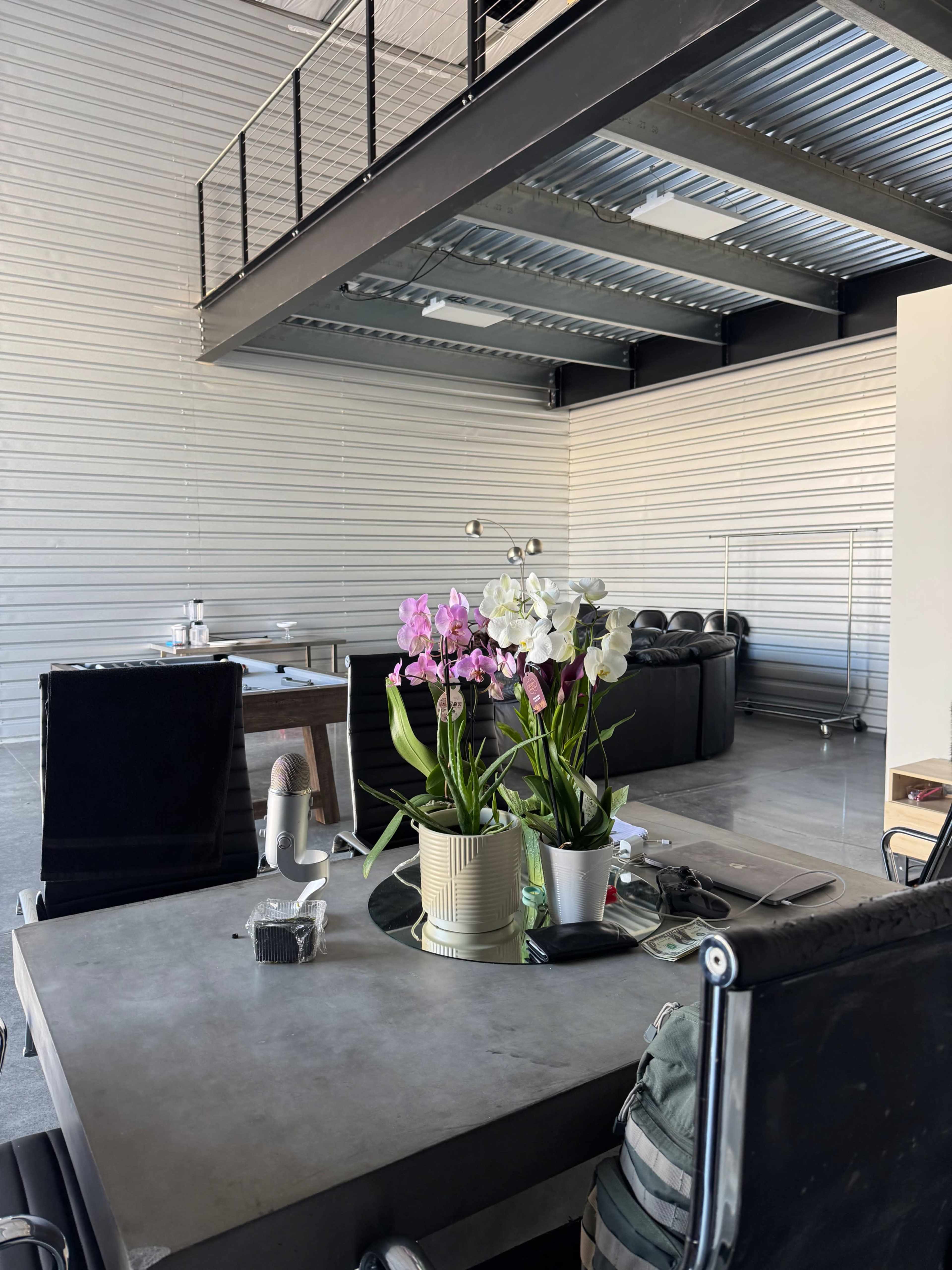 The image shows a modern office space featuring a table with potted orchids, a black chair, and a minimalistic interior design.