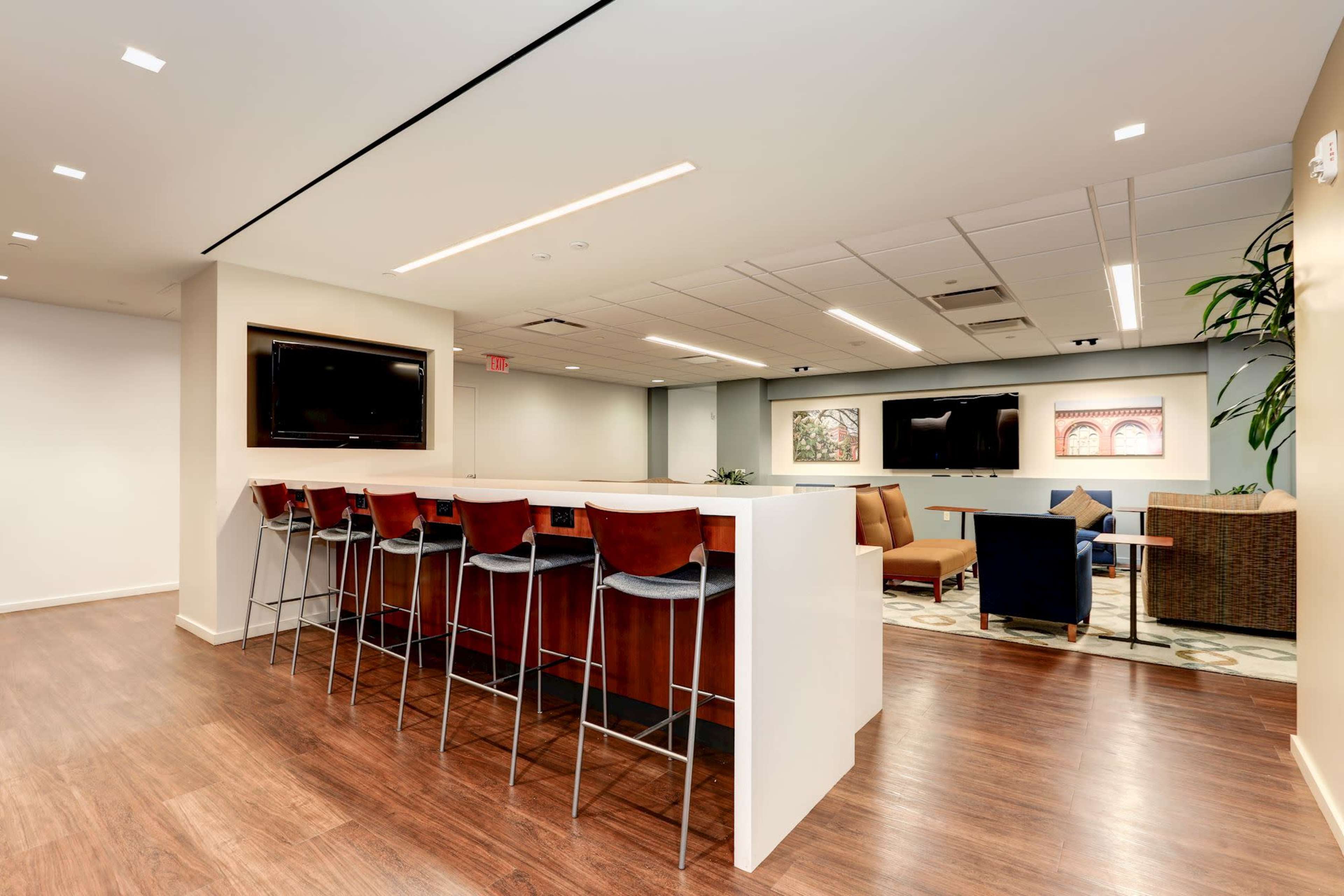 A modern office lounge area with a bar-height counter, seating, and multiple television screens on the walls.