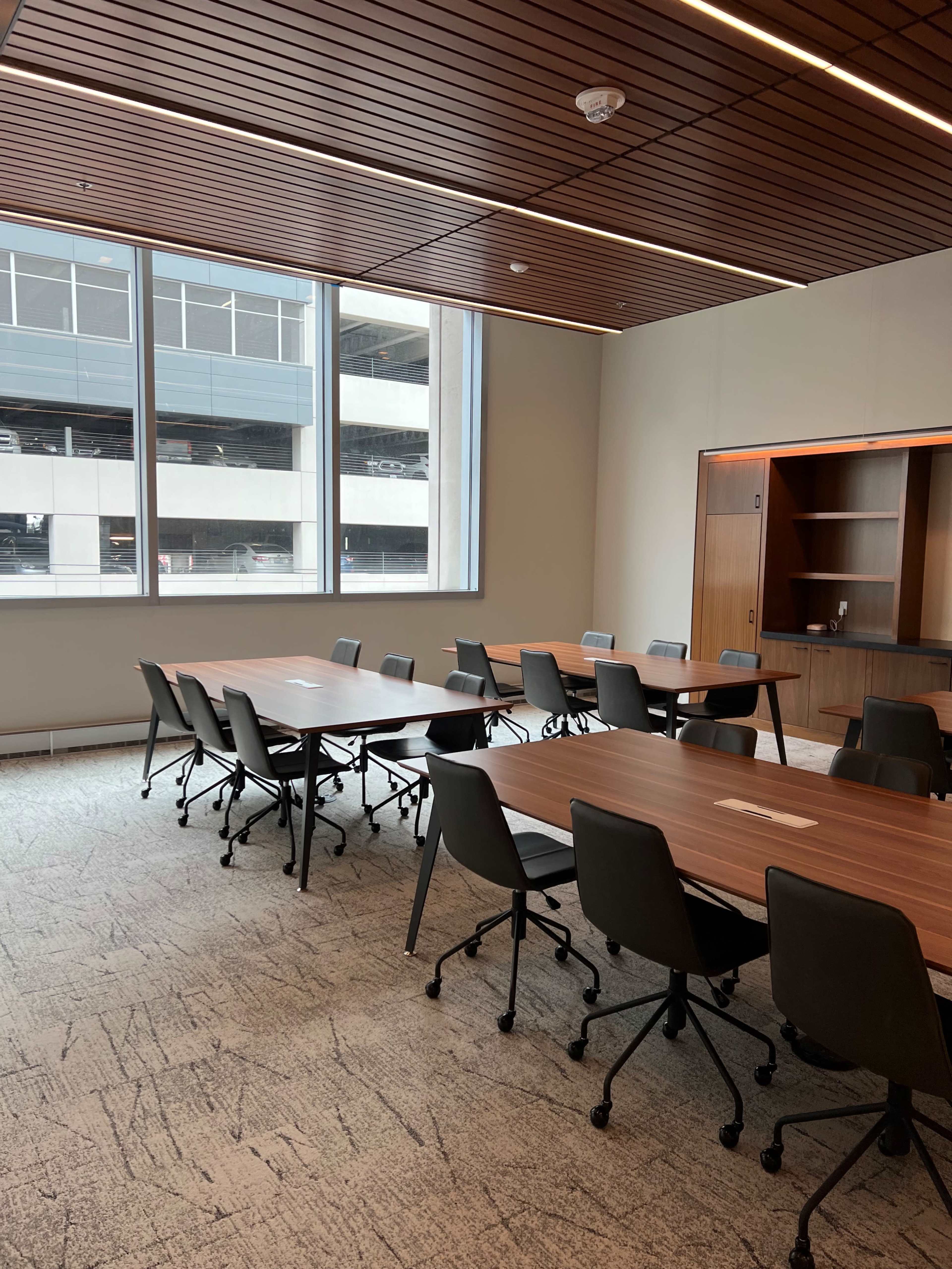 The image shows a modern conference room with multiple tables arranged in a U-shape and large windows providing natural light.