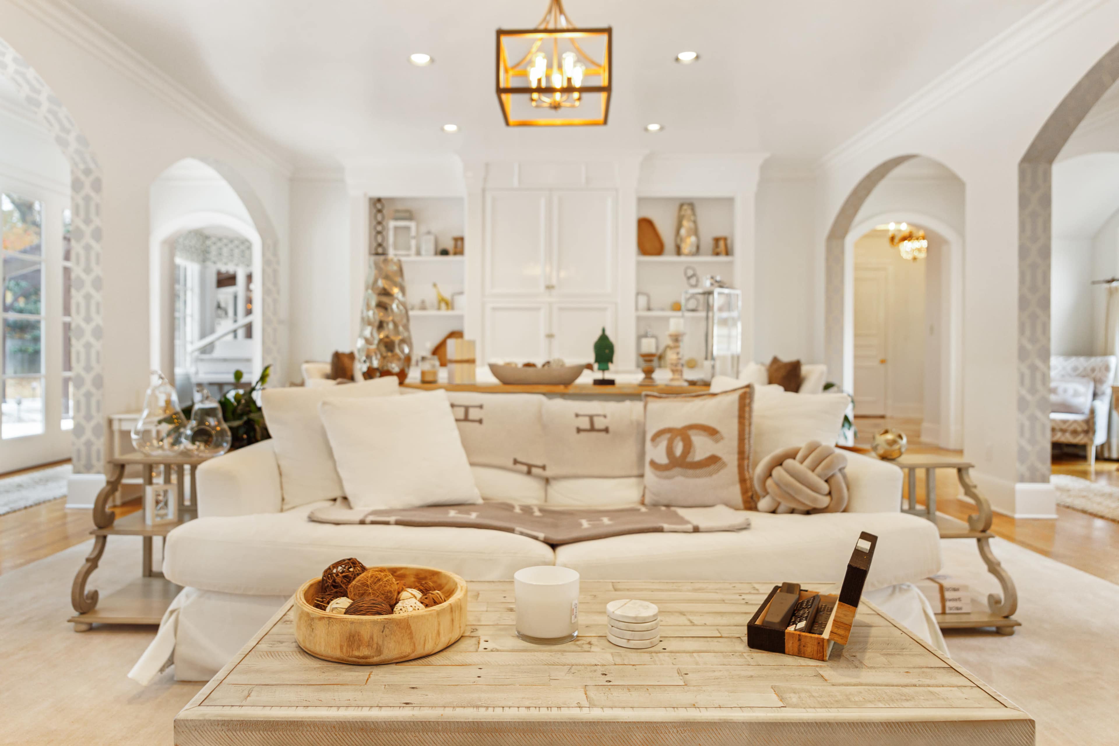 The living room features a sofa adorned with decorative pillows, a coffee table with a wooden bowl and a candle, and an archway leading to another space.