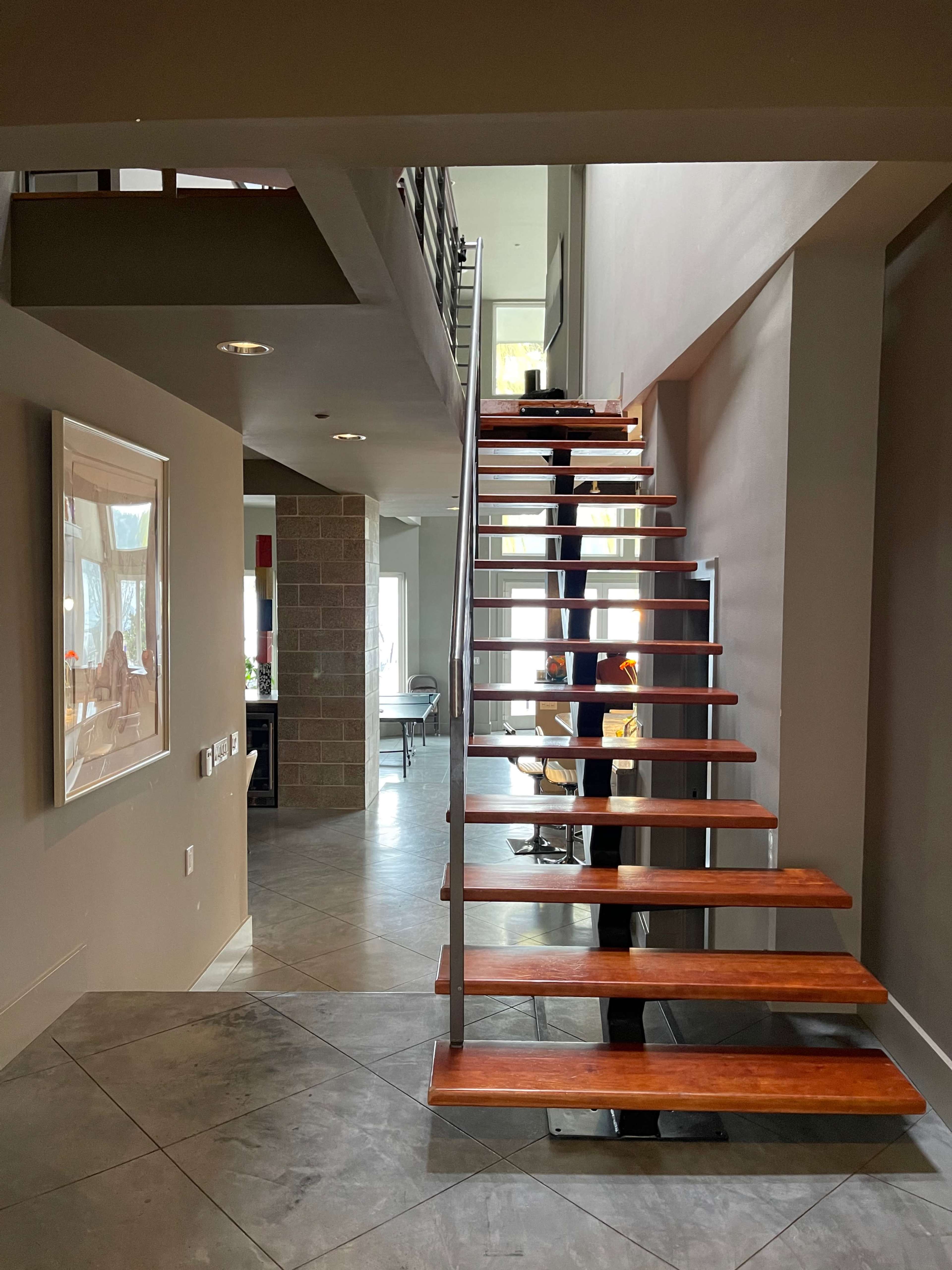The image shows a modern staircase with wooden steps leading to a second floor in a bright, open space.