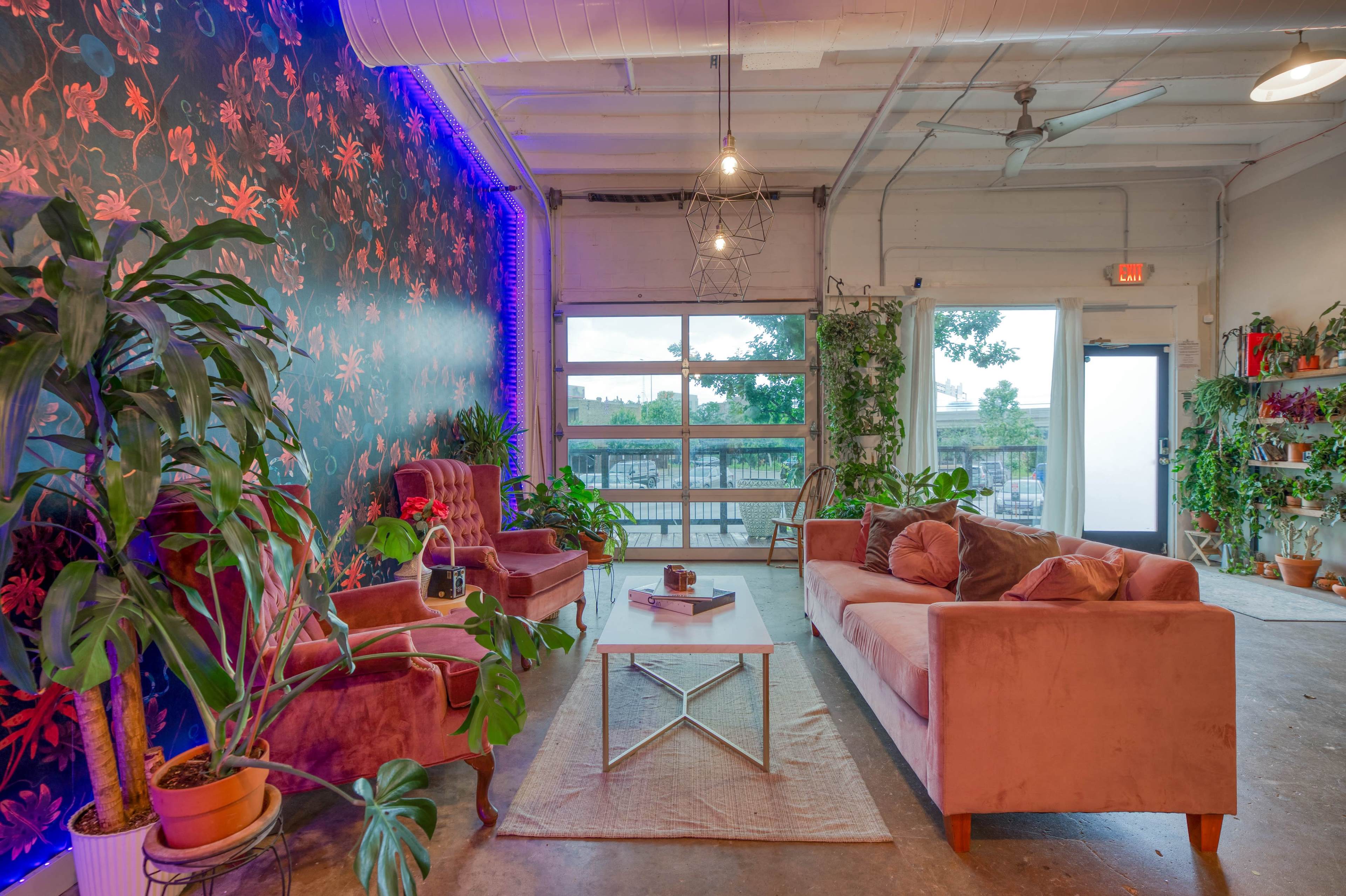 A stylish lounge area with pink velvet furniture, a patterned floral wall, and large windows that allow natural light to fill the space.