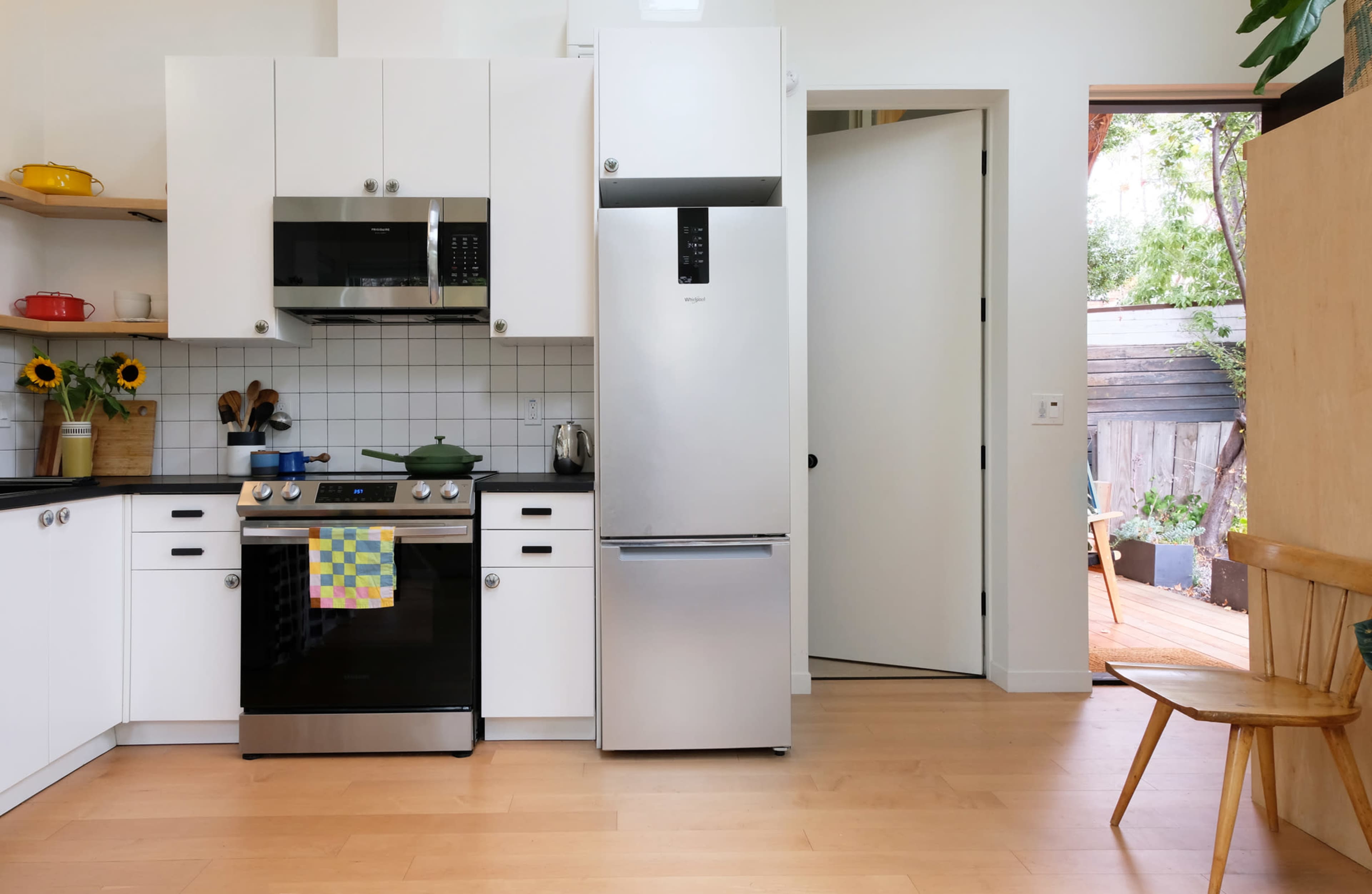 A modern kitchen features stainless steel appliances, white cabinetry, and a view of an outdoor space through an open door.