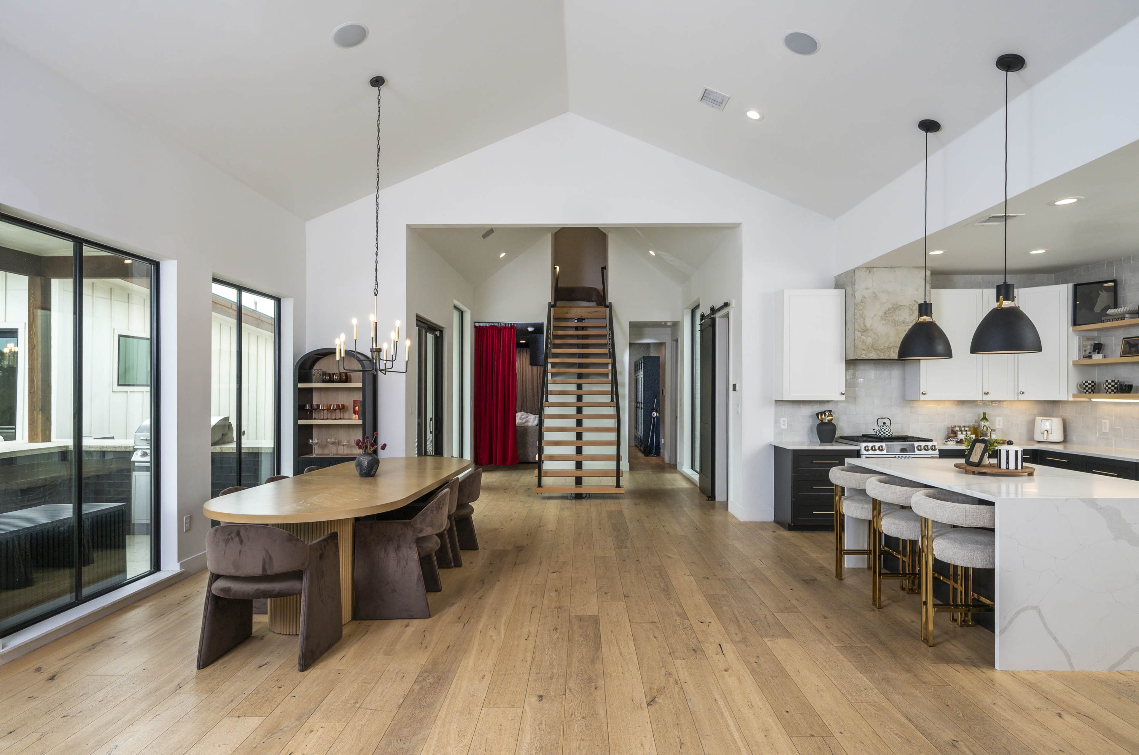 The image shows a modern open-concept living space with a dining area, a kitchen featuring bar stools, and a staircase leading to an upper level.