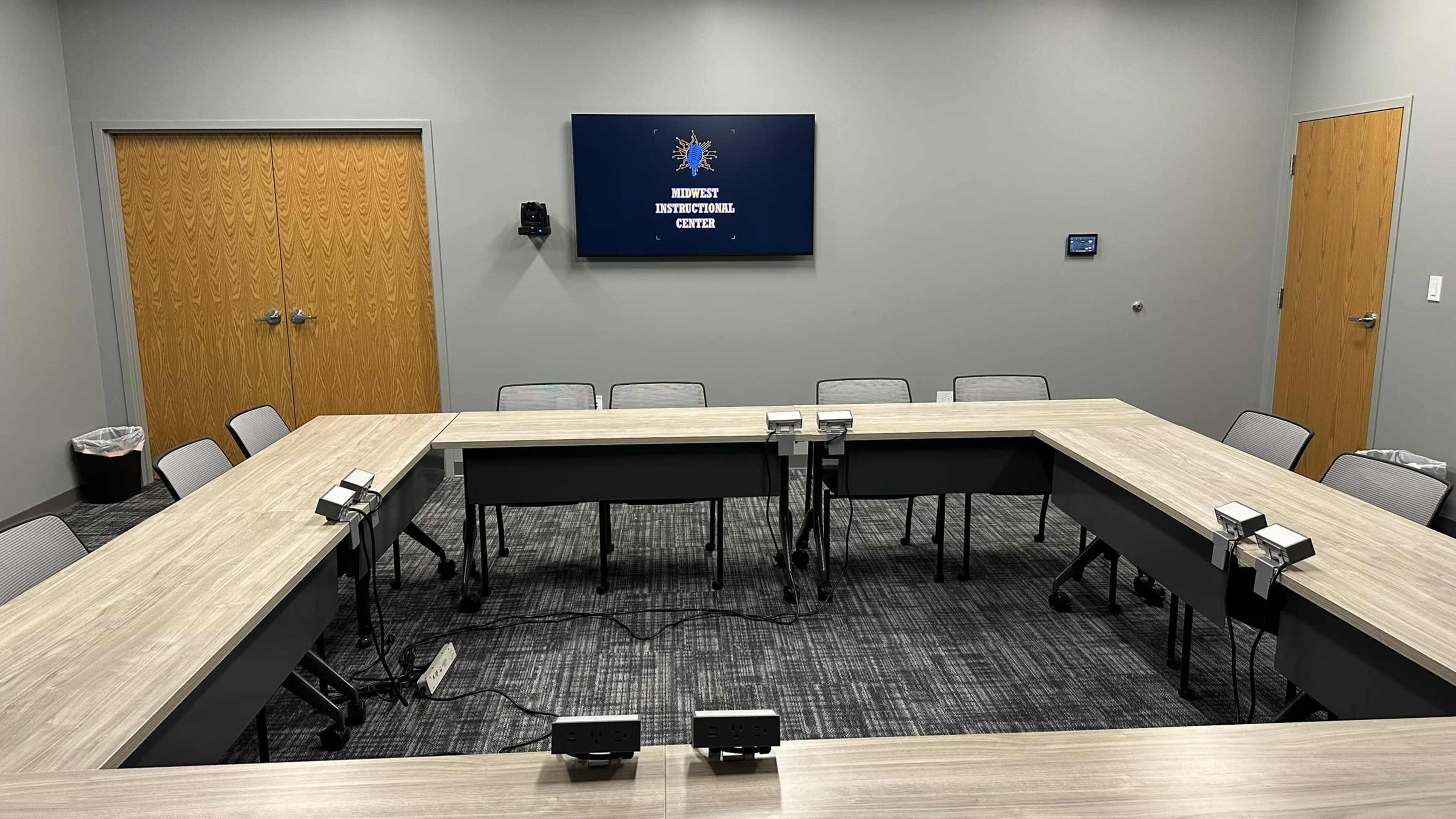 A modern conference room features a rectangular table, multiple chairs, and a large screen mounted on the wall.