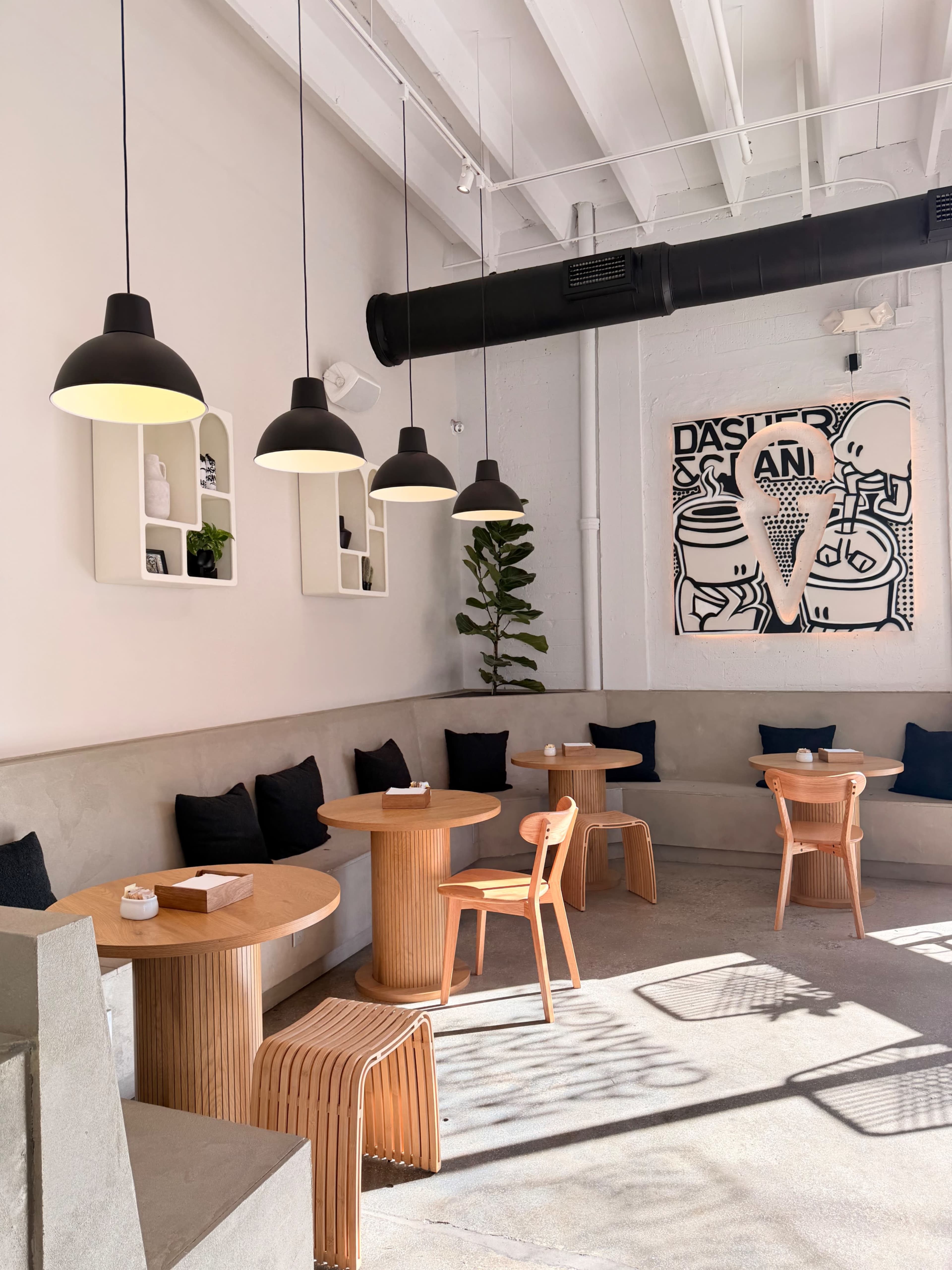 The scene shows a modern café with wooden tables and chairs, black pendant lights, and a decorative wall featuring an ice cream-themed artwork.