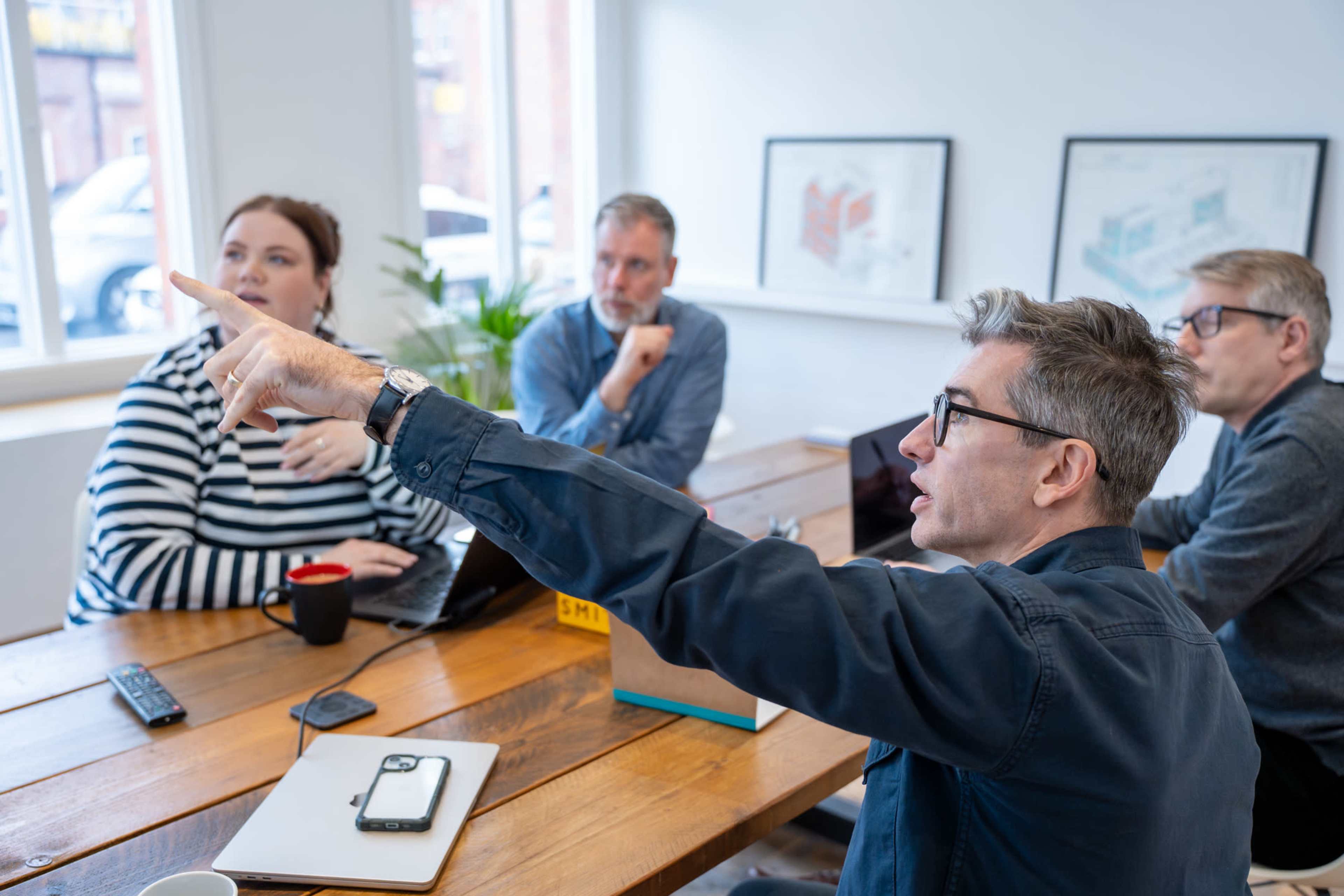 A group of four professionals is engaged in a discussion around a wooden table in a bright meeting room.
