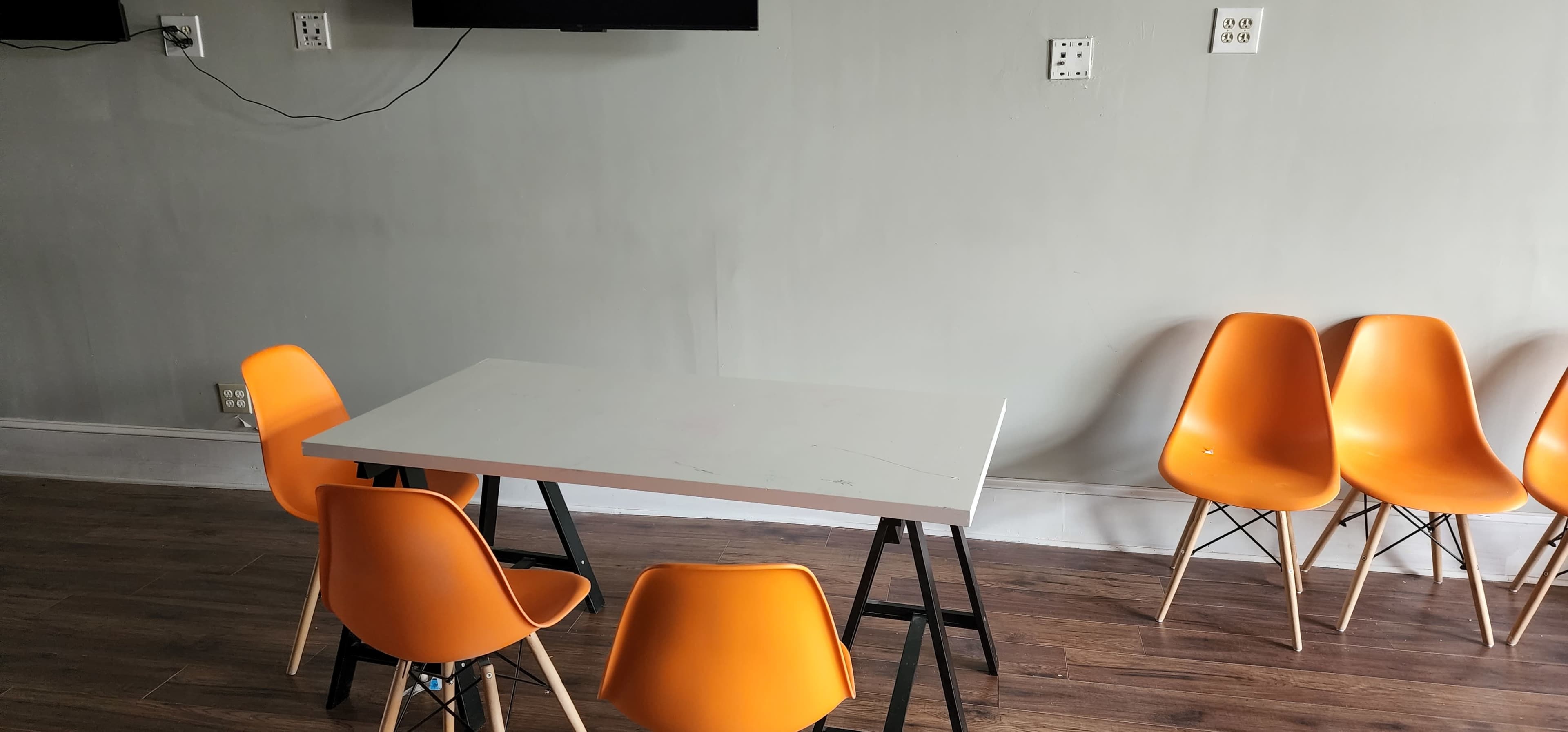 A white table with black legs is placed in a room with six orange chairs arranged around it.
