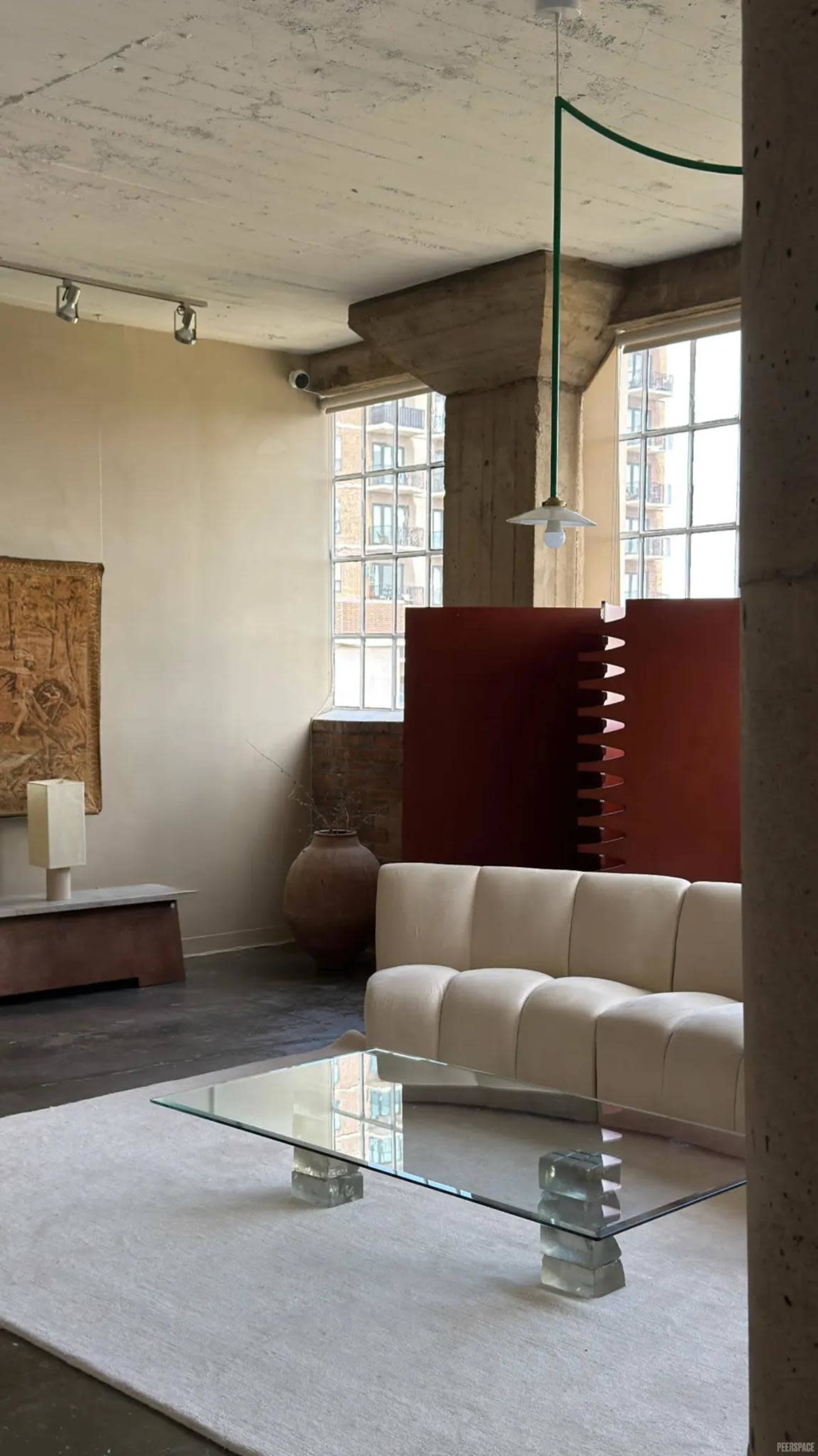The image shows a minimalist living room with a white curved sofa, a glass coffee table, and large windows providing natural light.