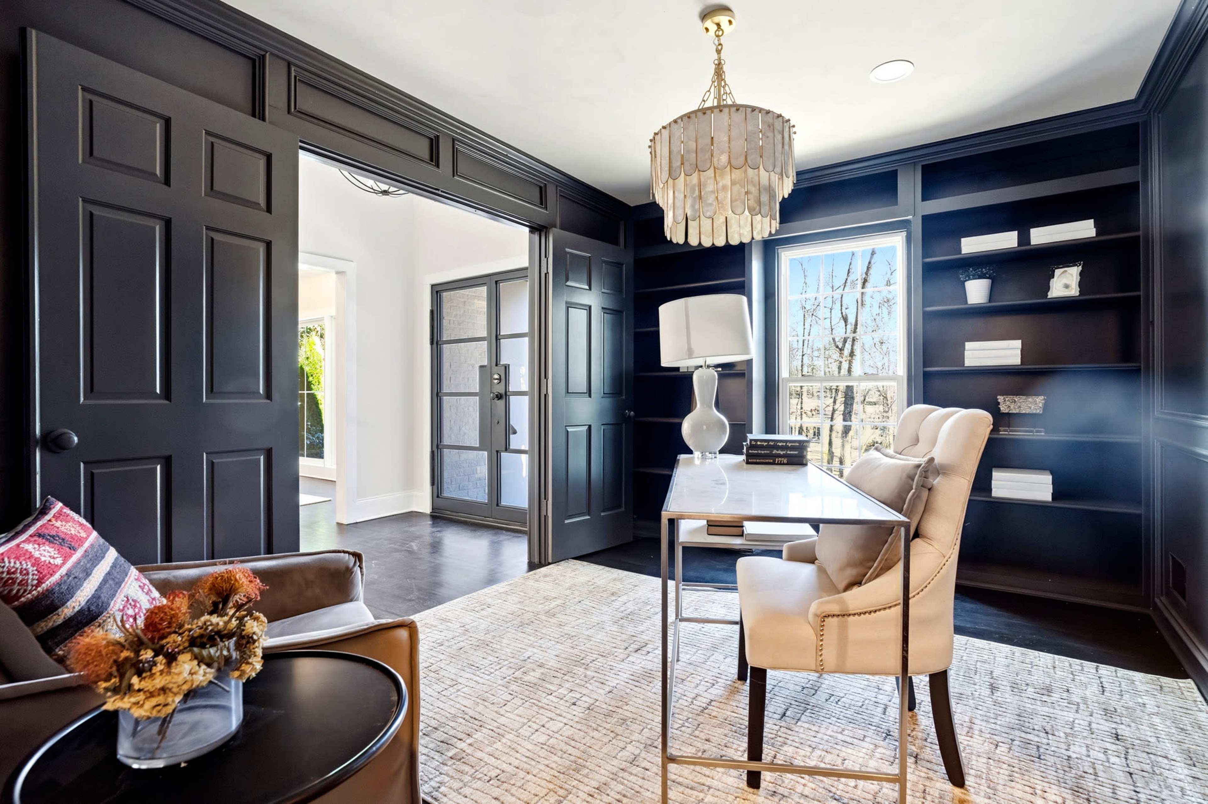 The image shows a dark-painted home office featuring a desk with a lamp, a comfortable chair, and built-in shelves.