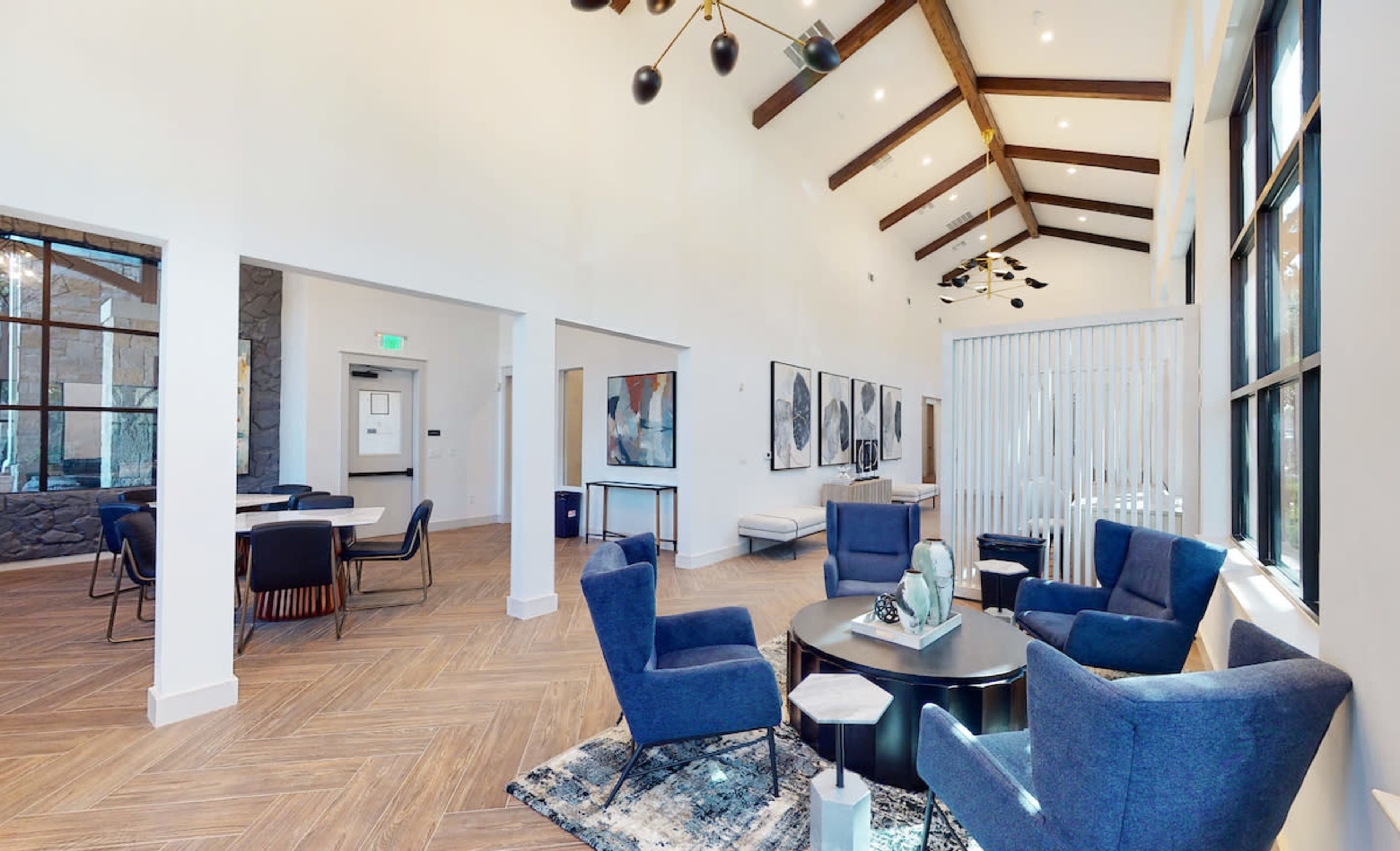 A spacious lounge area featuring modern furniture, high ceilings with wooden beams, and large windows.