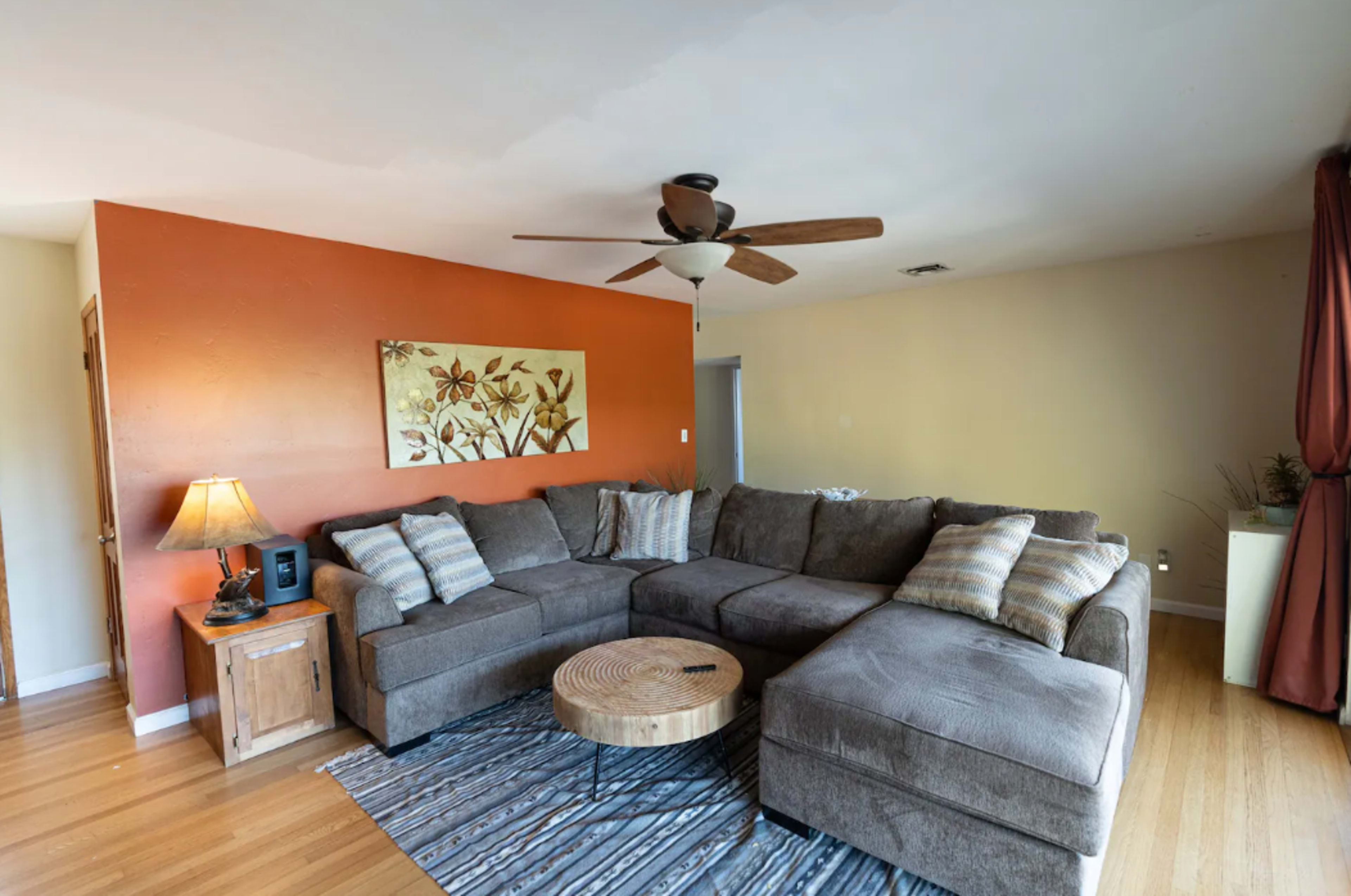 A living room featuring a large sectional sofa, a circular wooden coffee table, a floor lamp, and an orange accent wall.