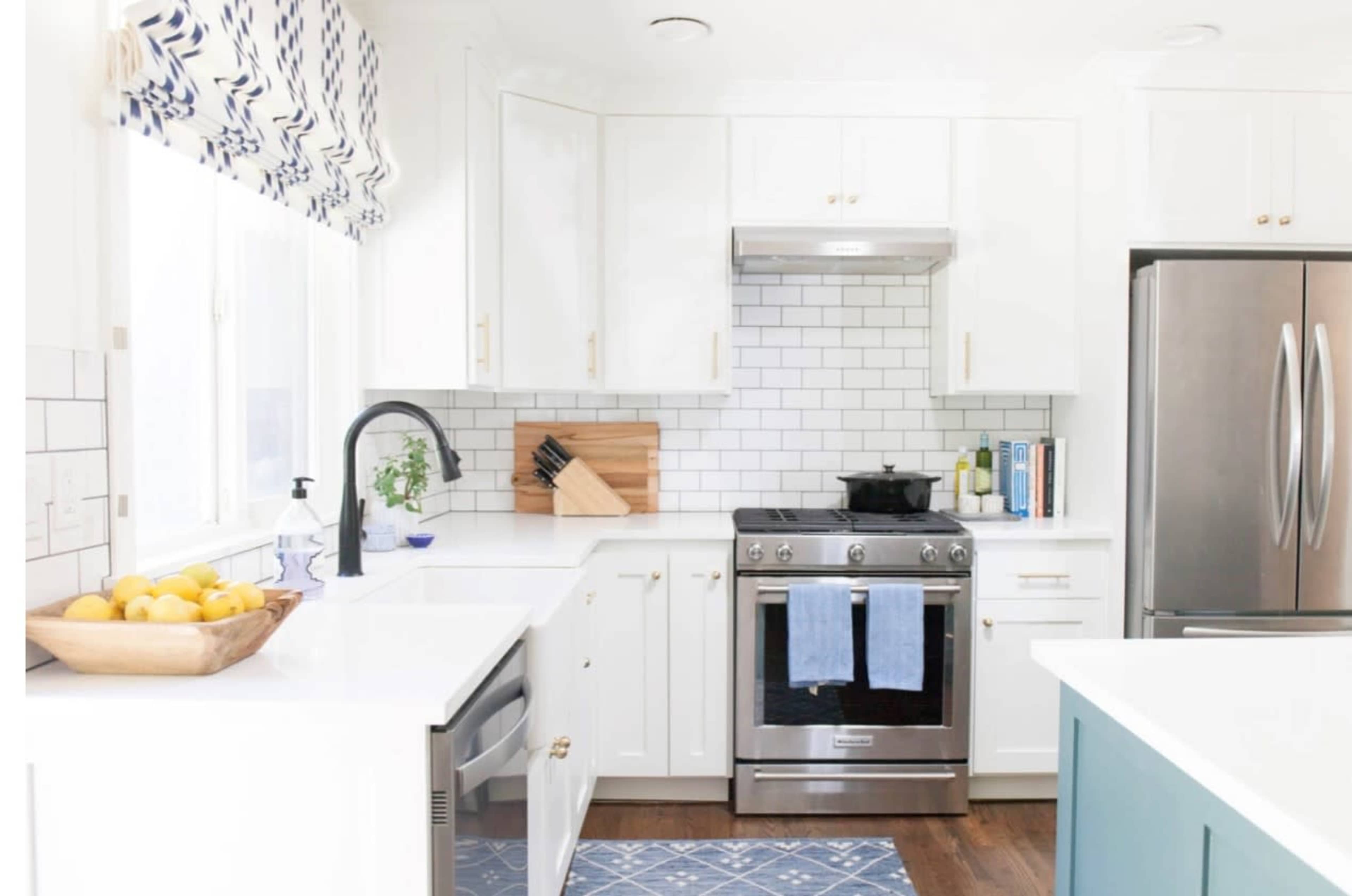 A modern kitchen featuring white cabinets, a stainless steel stove, a blue dish towel, and a bowl of lemons on the counter.