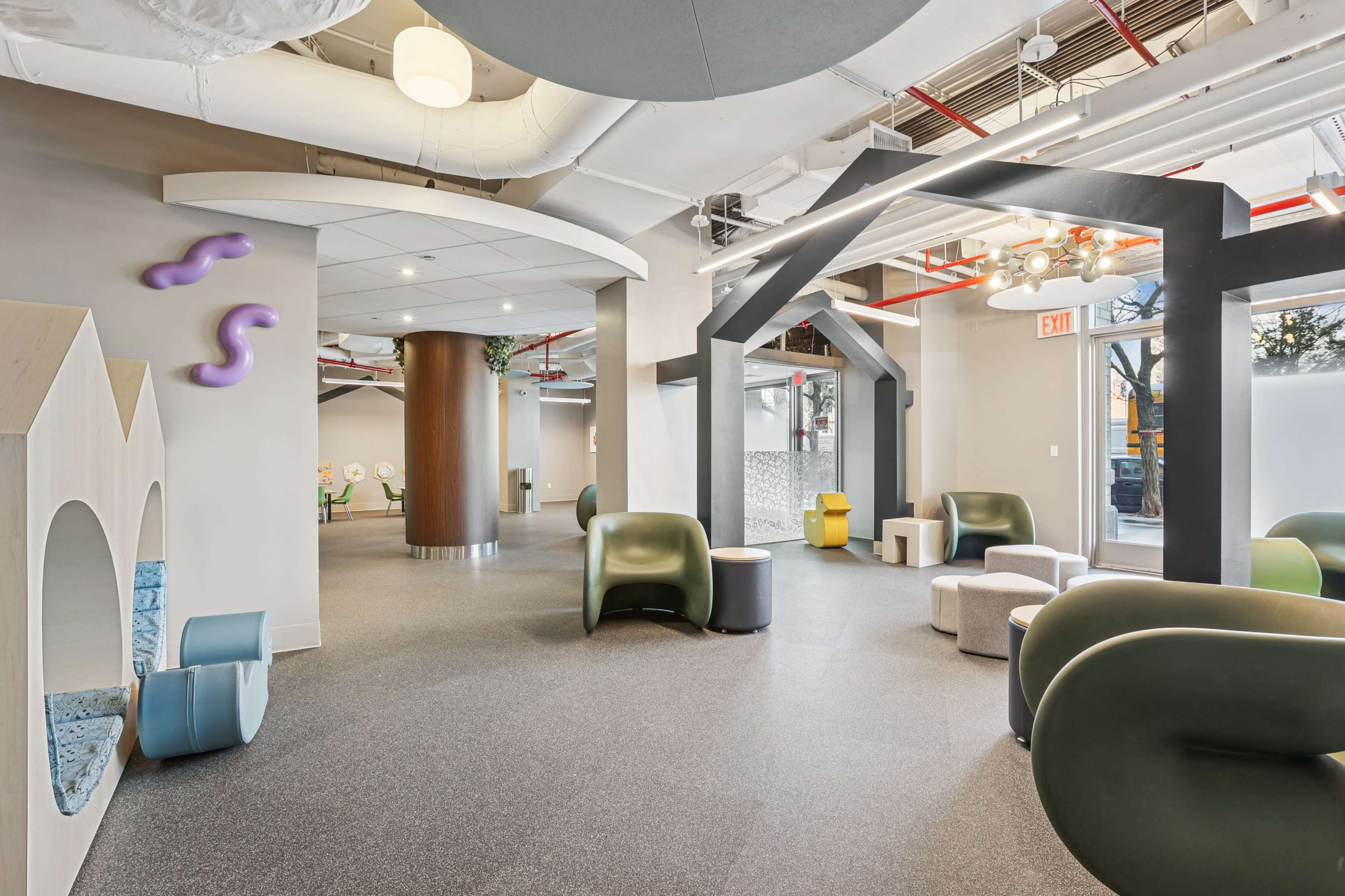 The image shows a modern, open space featuring a variety of seating options and playful architectural elements, with large windows allowing natural light to enter.