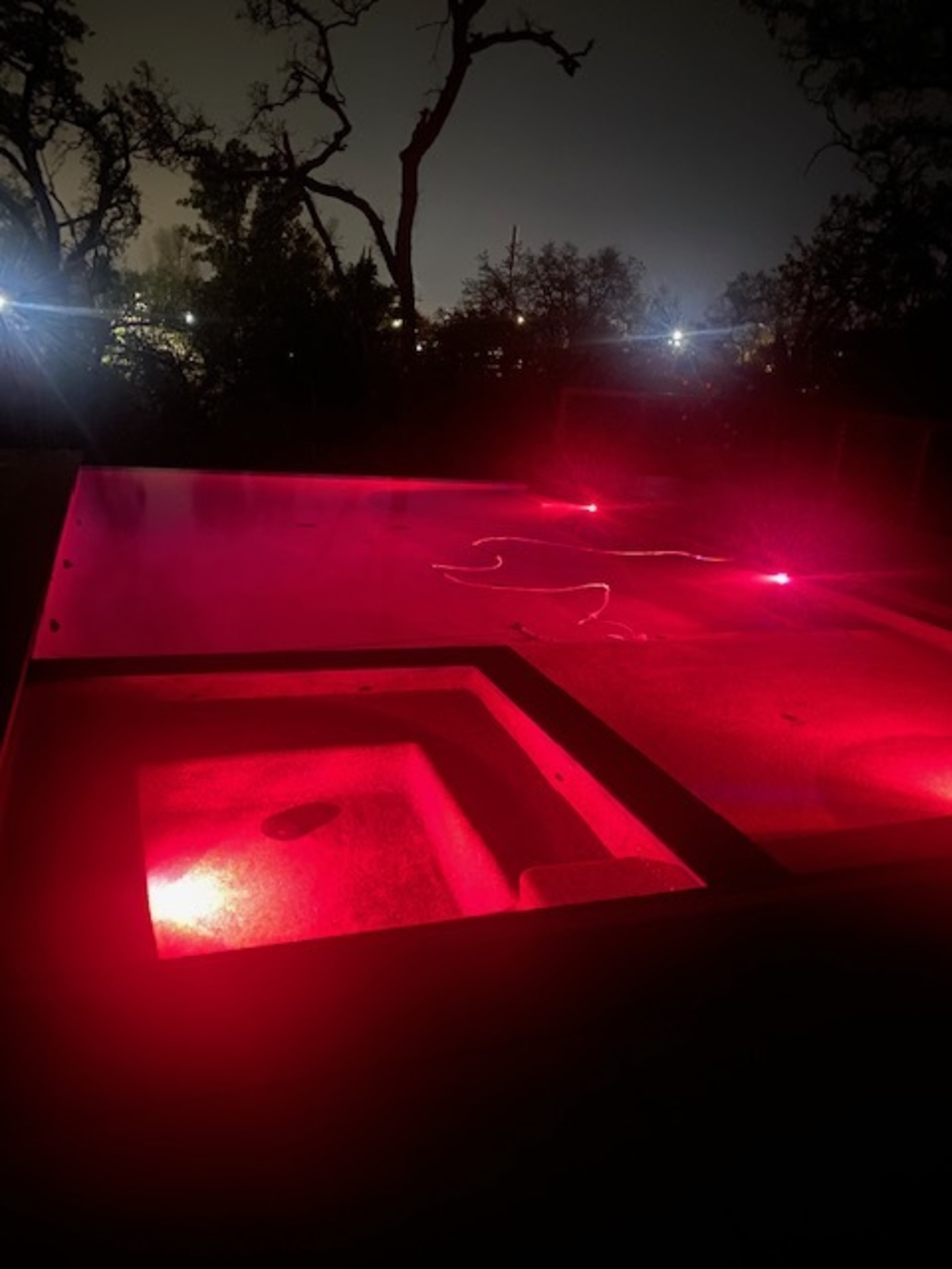 A lit pool at night, with a red light illuminating the water and surrounding area.