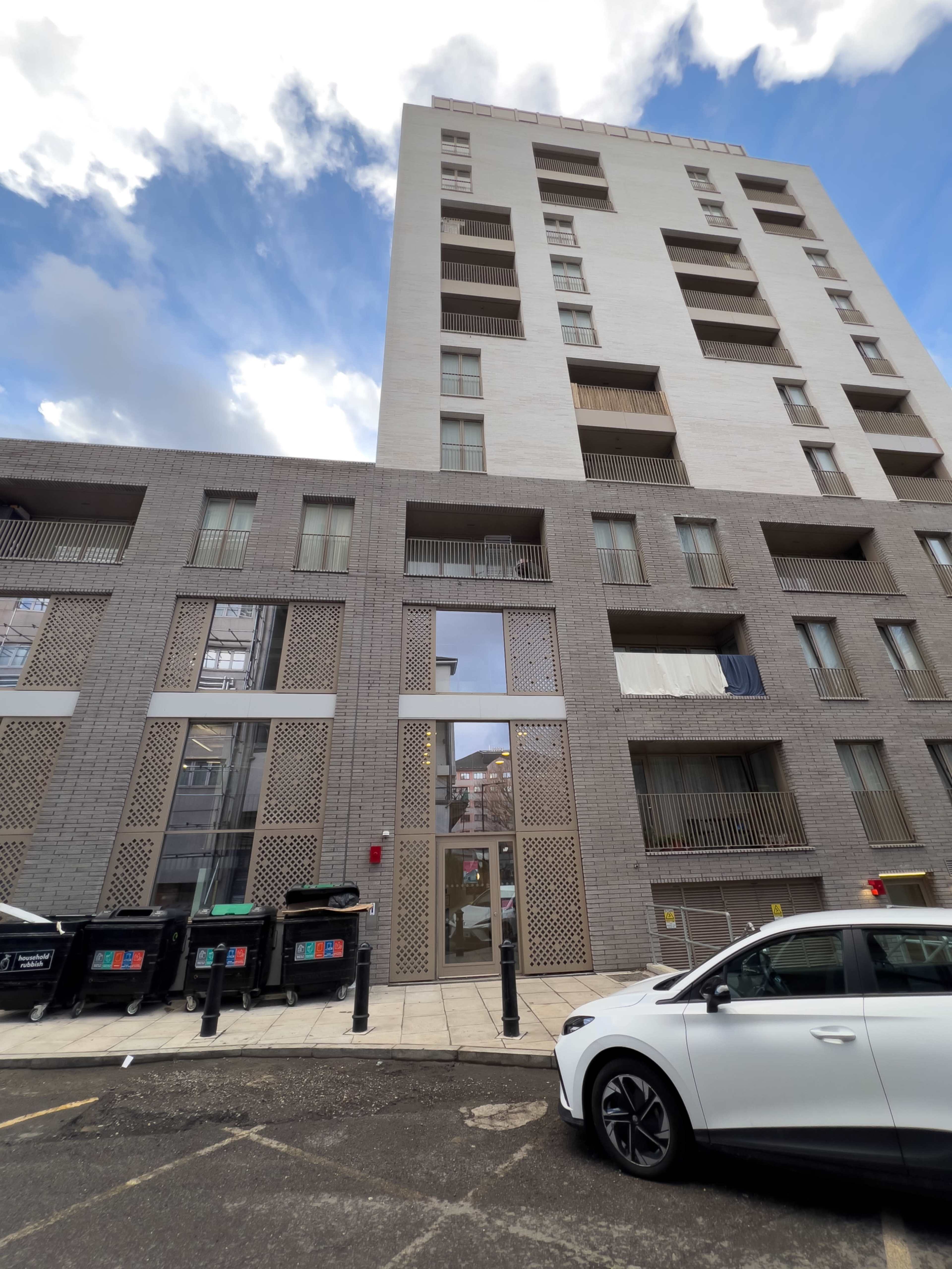 A multi-story residential building featuring a combination of light and dark exterior materials, with balconies and large windows on the lower levels.