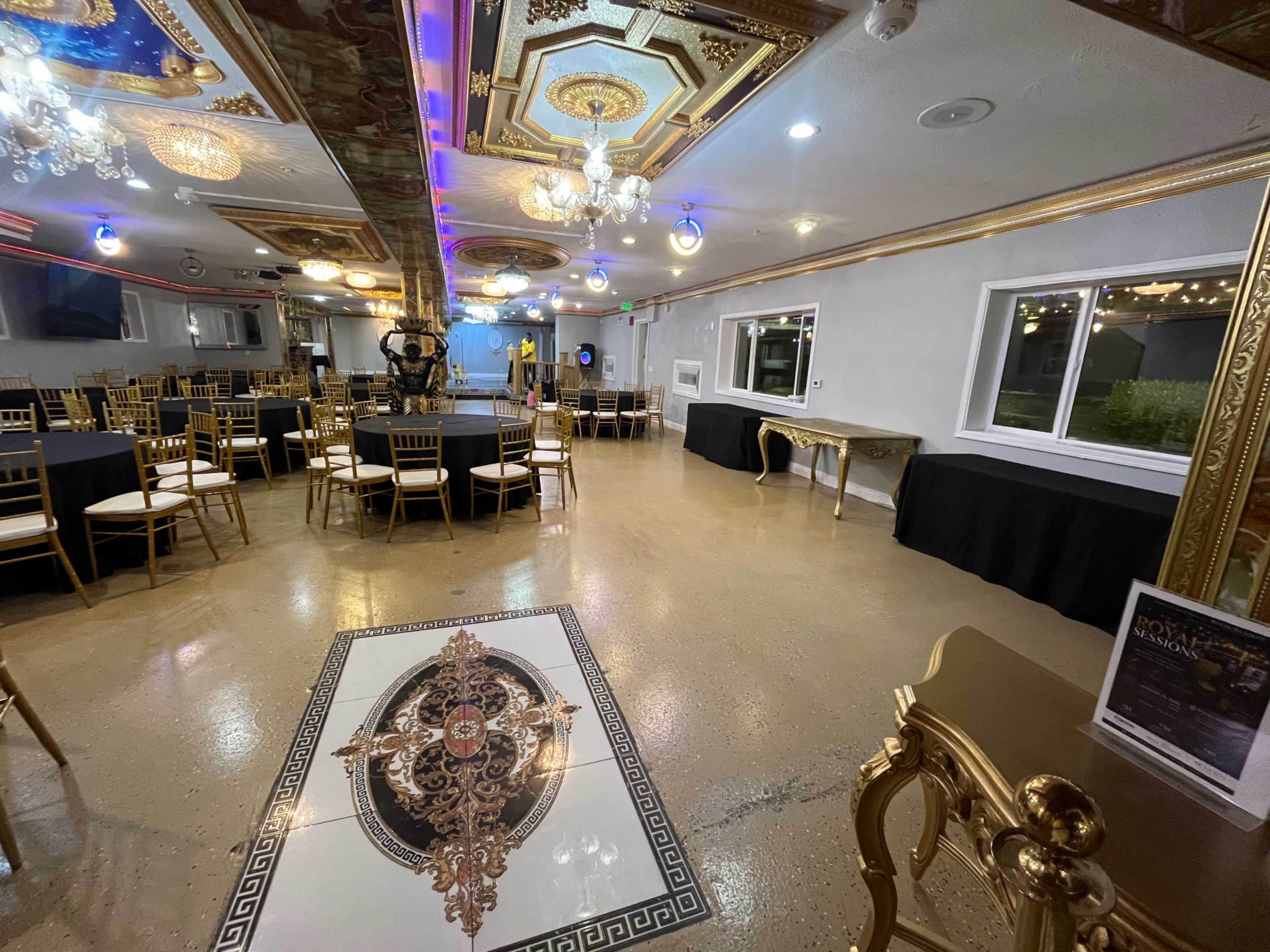 The image shows a banquet hall with gold-accented furniture, round tables set with chairs, and elaborate ceiling decorations.