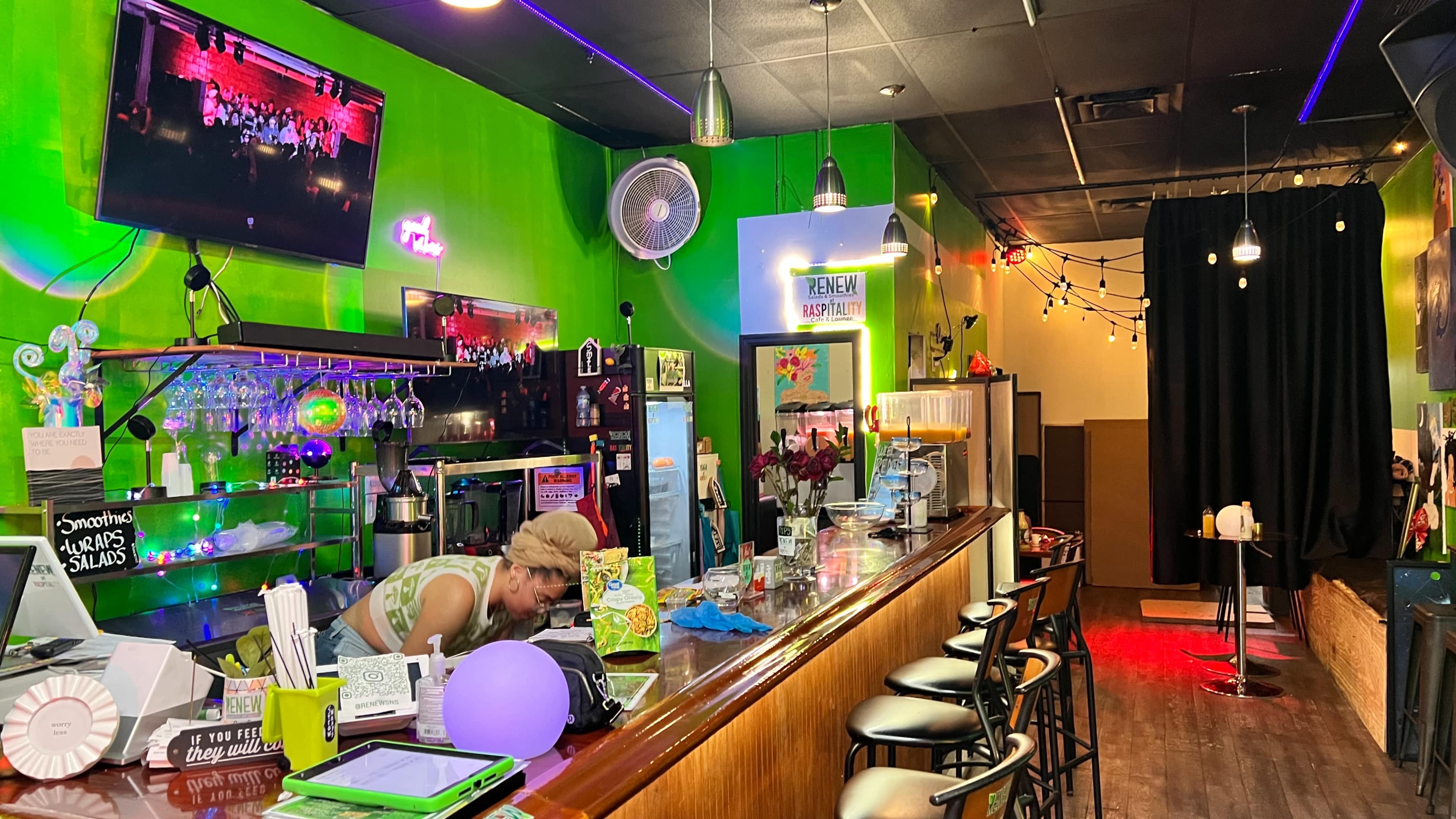 The image shows a vibrant bar scene featuring a bartender arranging drinks and colorful decor, with a neon green wall and dim lighting creating a lively atmosphere.
