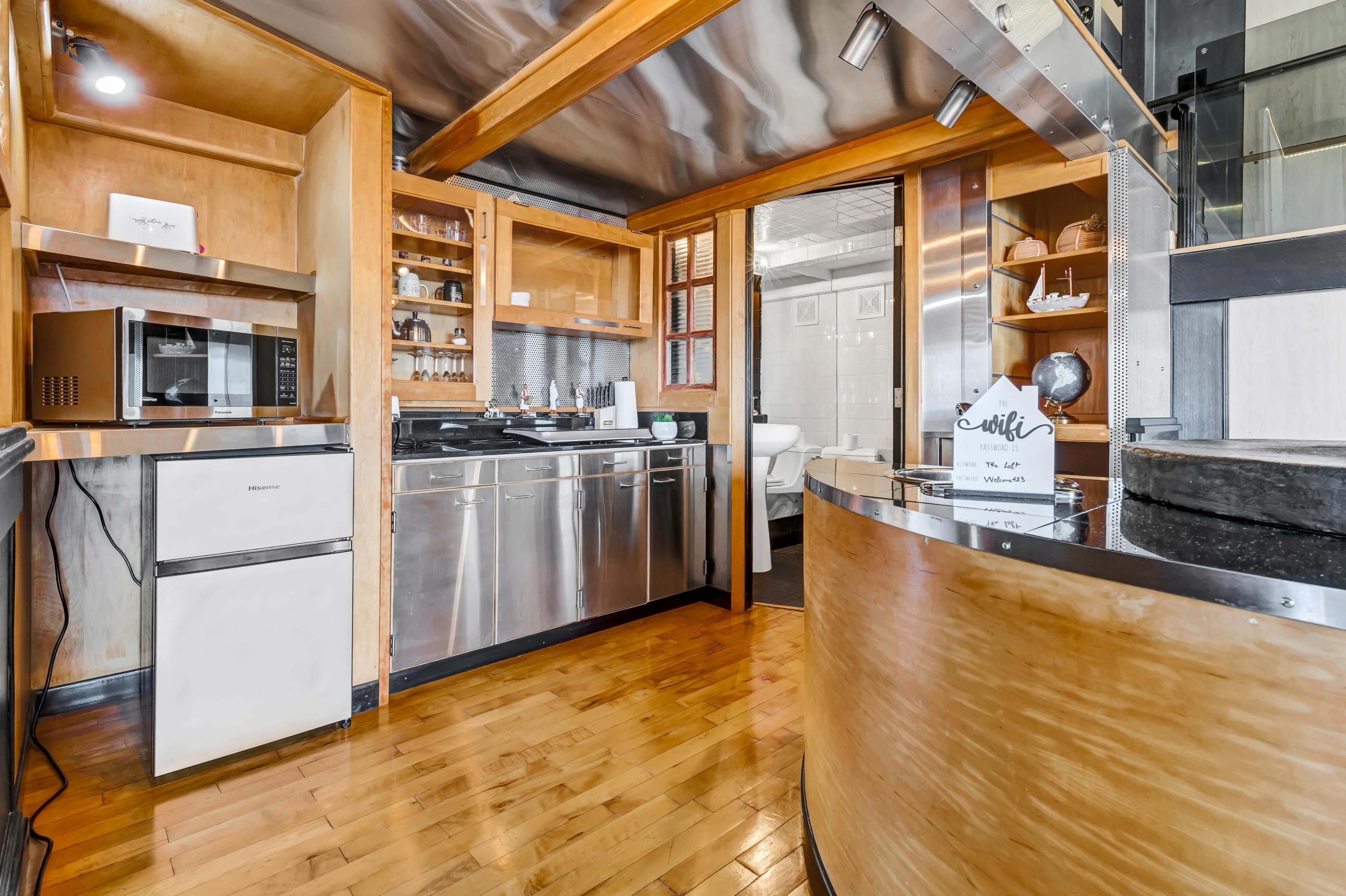 A modern kitchen with wooden cabinetry, stainless steel appliances, and an open layout connecting to another room.