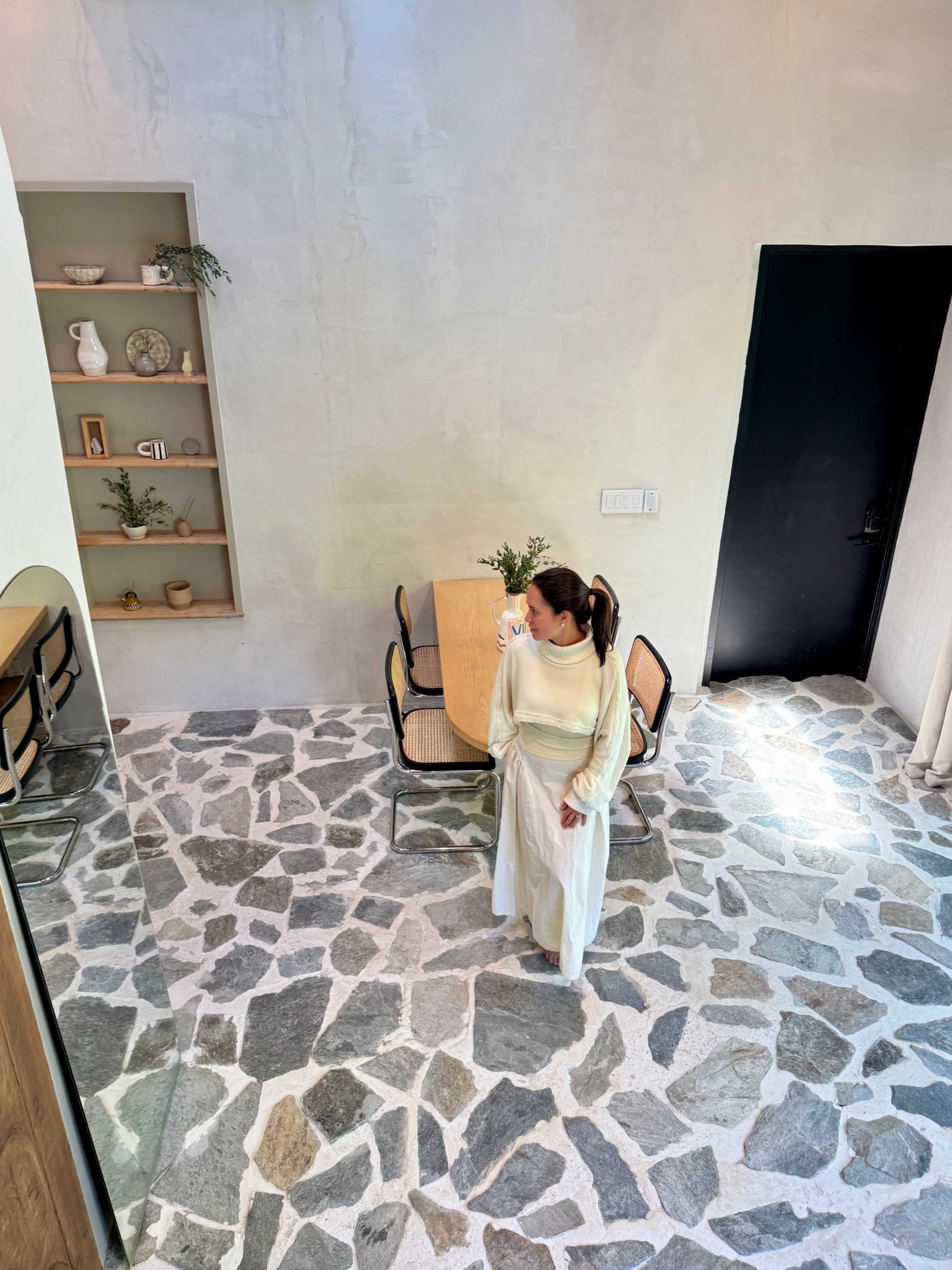 A woman stands in a modern interior space with a stone floor and a wooden dining table.