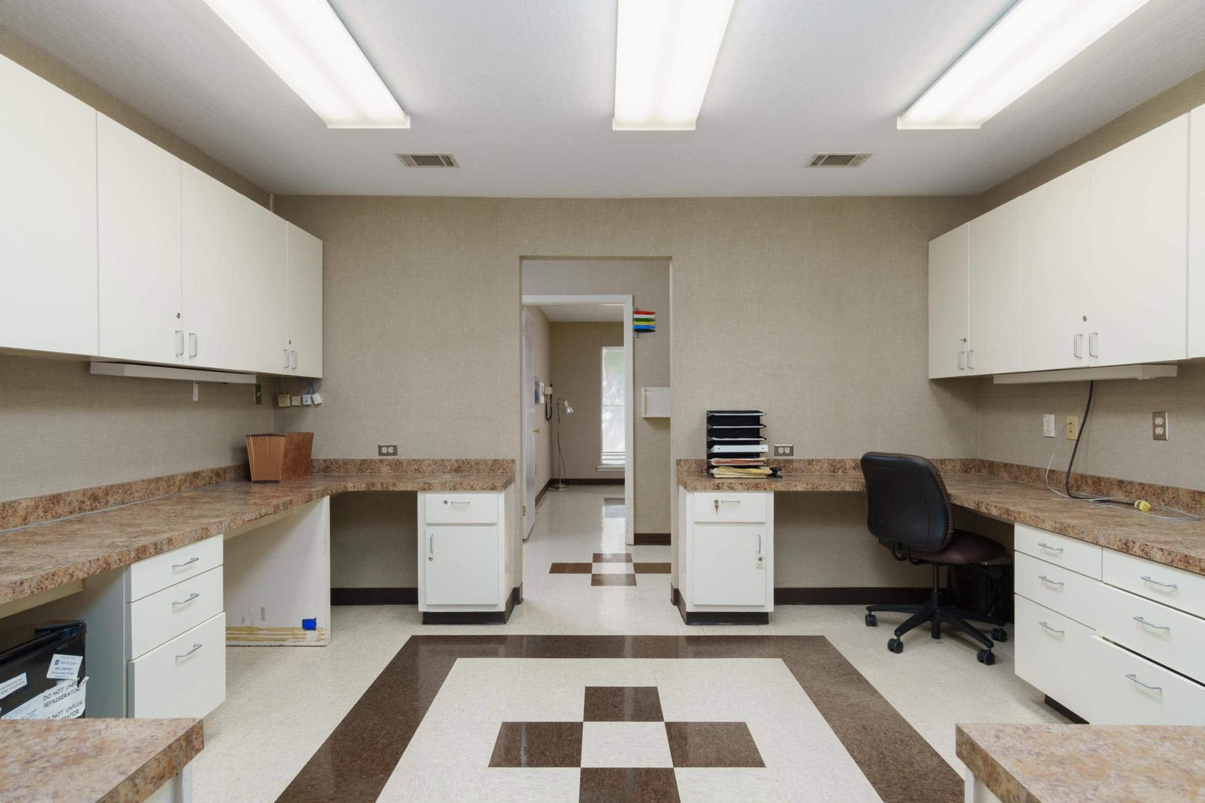 The image shows a tidy, well-lit room featuring beige walls, a patterned floor, and cabinets with a countertop on either side.