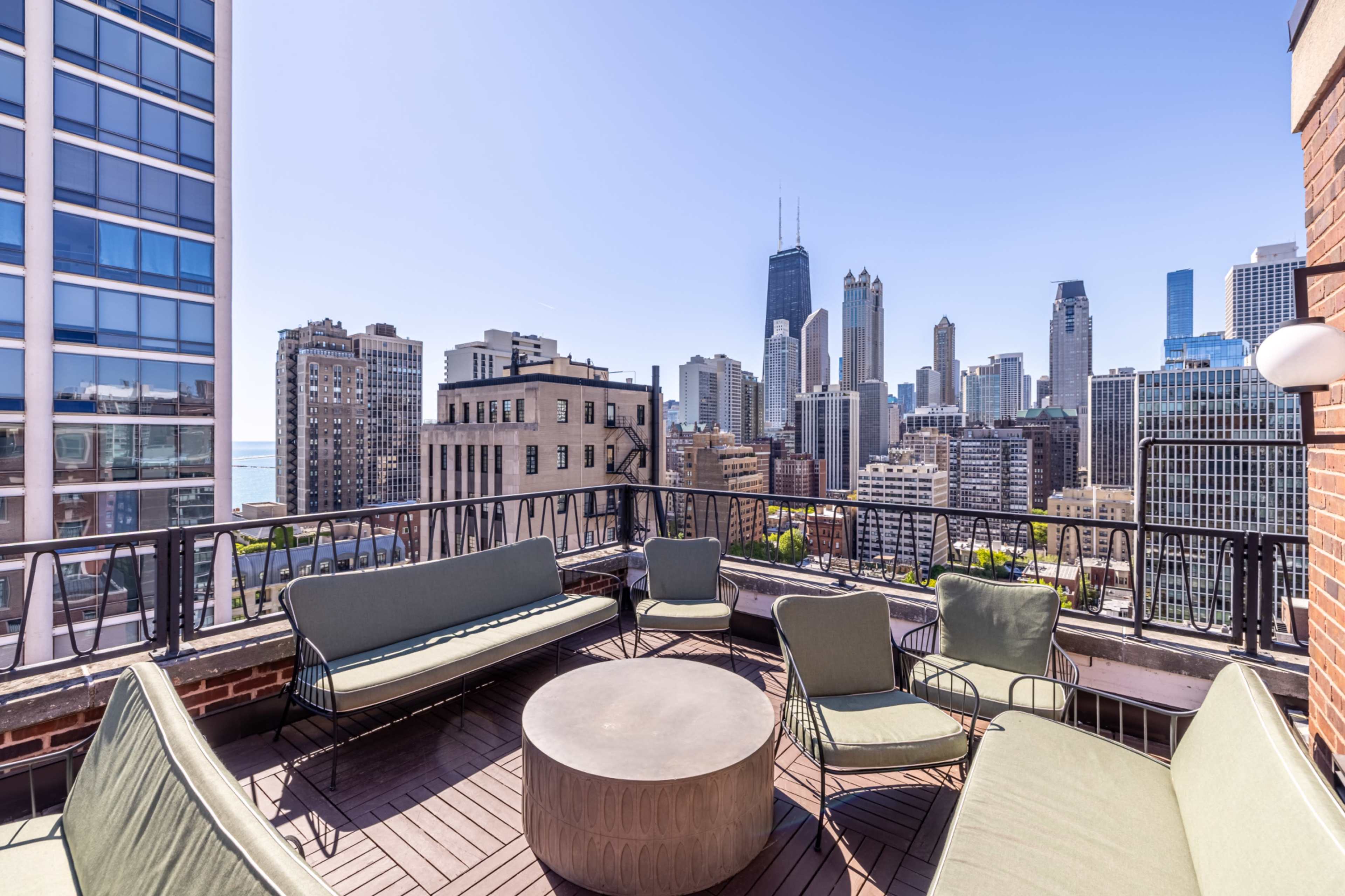 A rooftop patio with modern seating offers a panoramic view of a city skyline featuring skyscrapers against a clear blue sky.