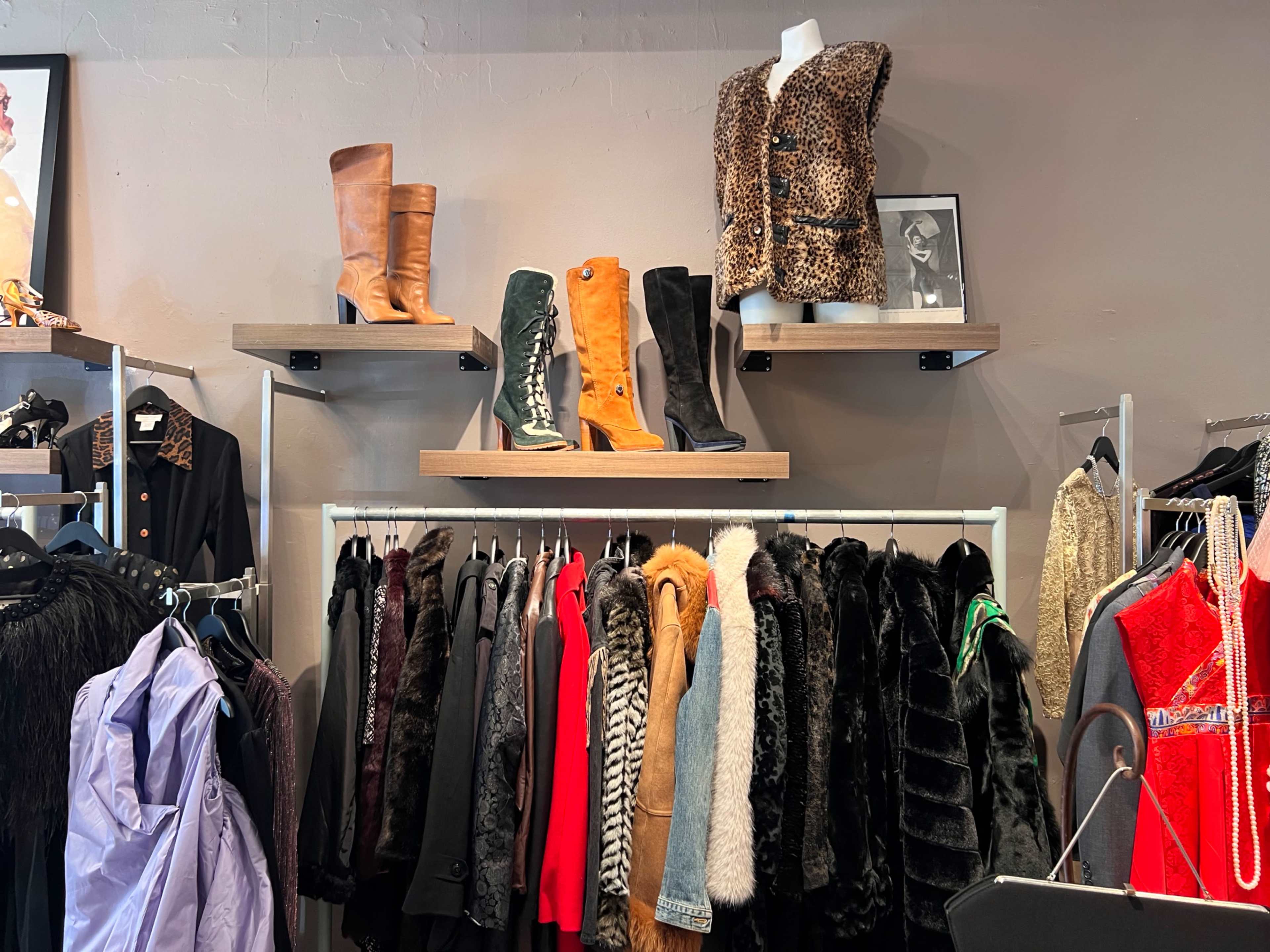The image shows a boutique interior with clothing racks filled with various garments and two shelves displaying boots and a leopard print vest.