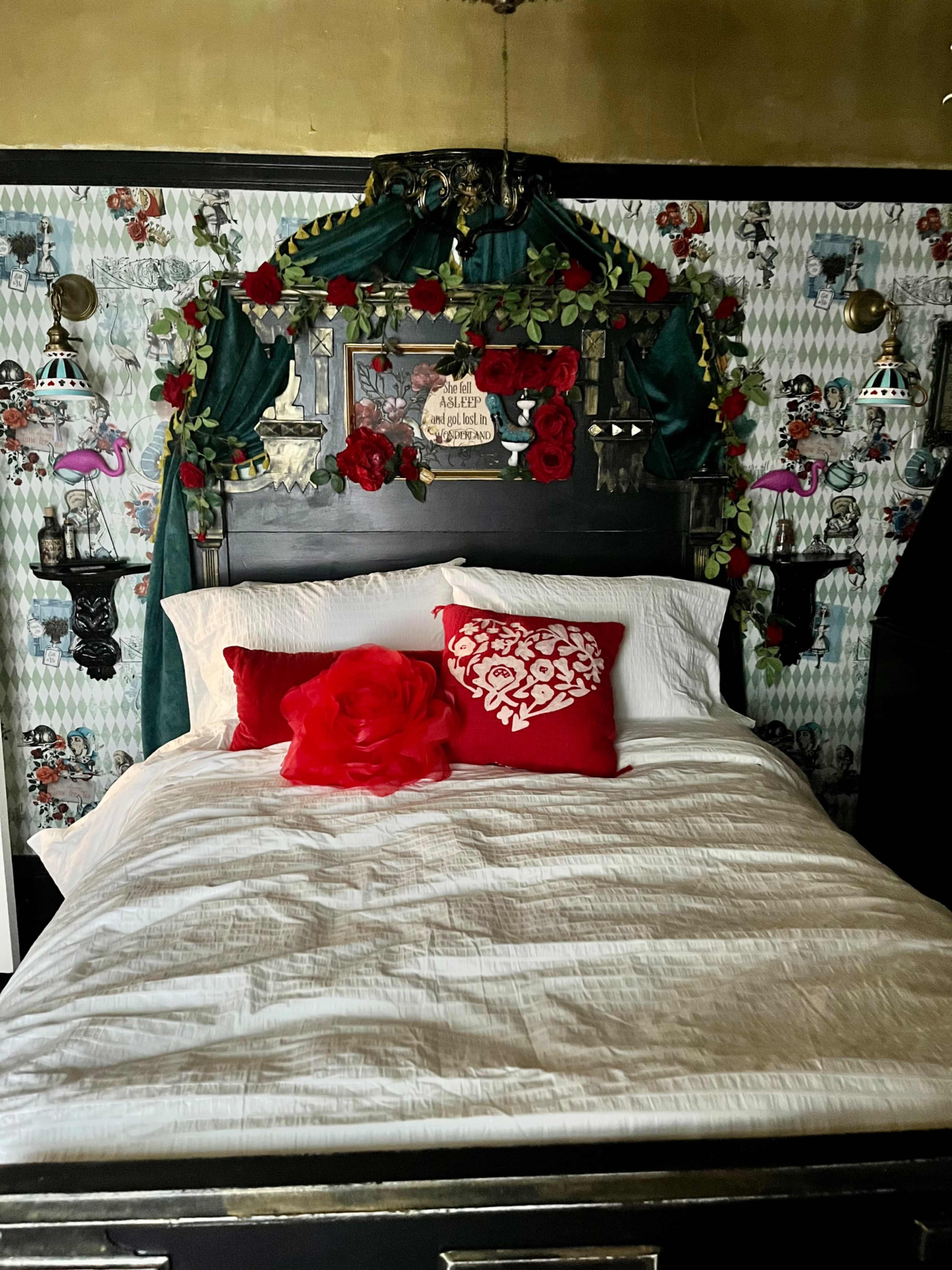 The image shows a bed with a decorative black headboard adorned with red roses and greenery, set against patterned wallpaper featuring playful designs.