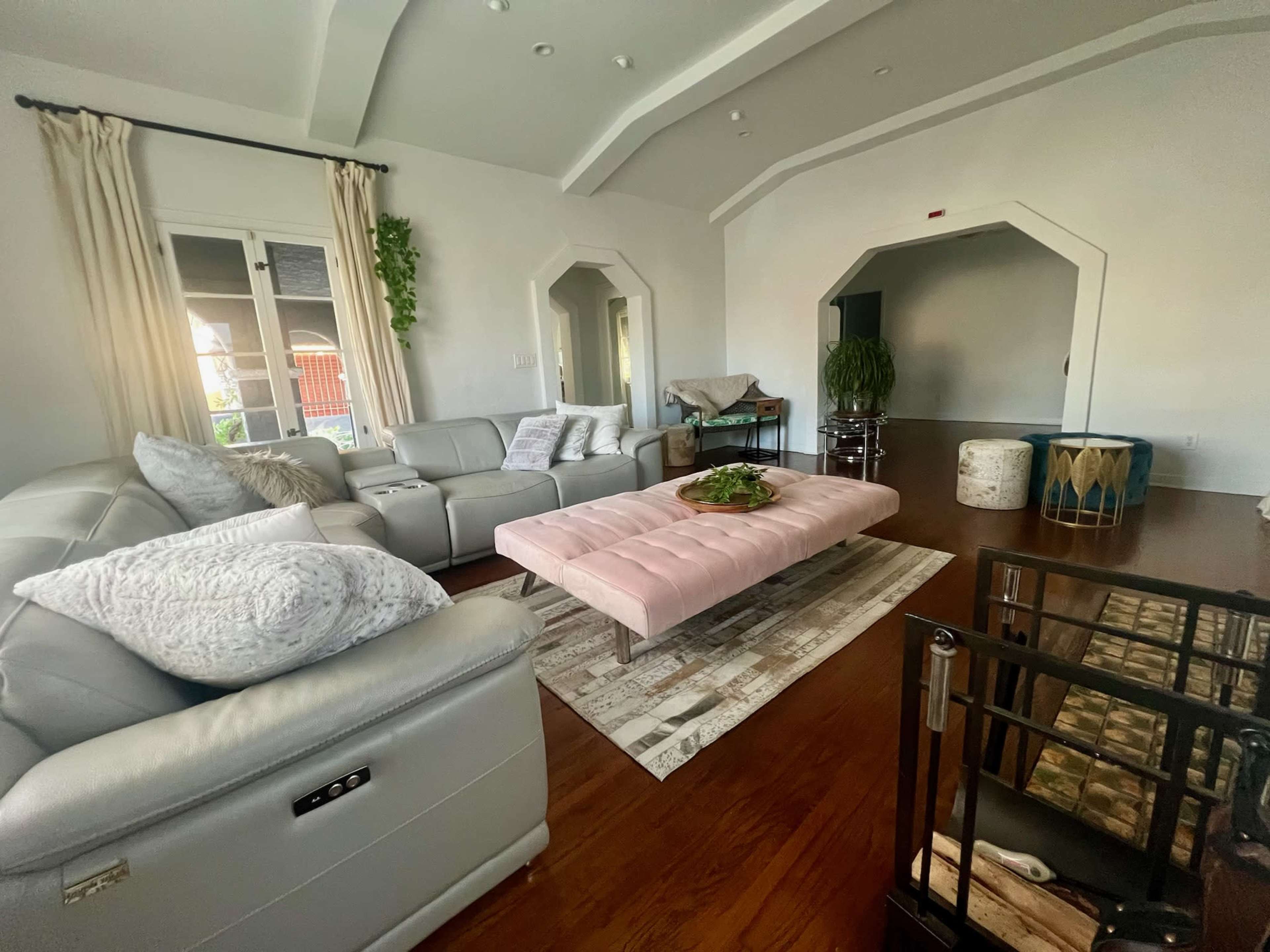 The image depicts a spacious living room featuring a large light pink coffee table, a grey sectional sofa, and modern decor elements.