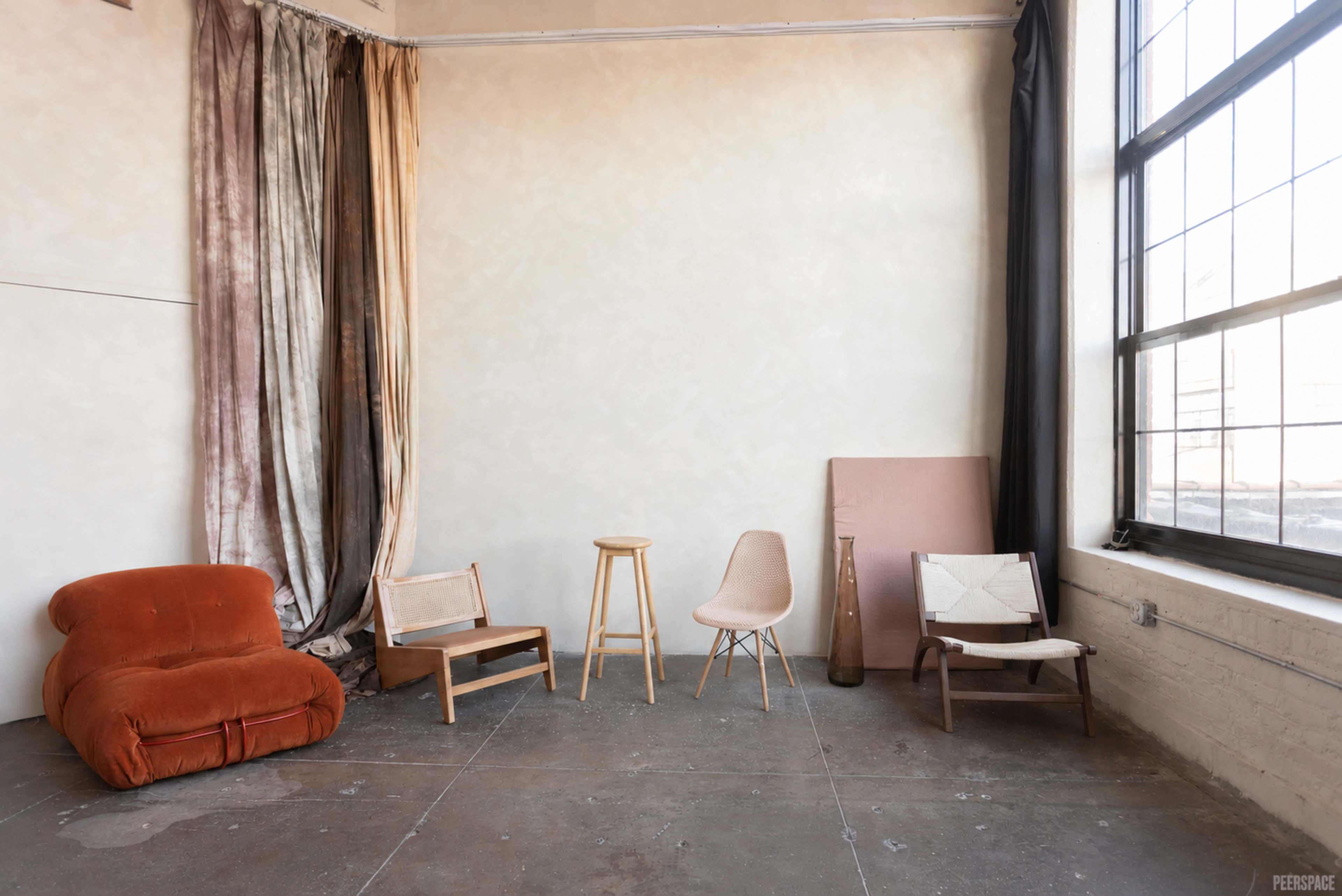 The image shows a minimalistic interior space with a mix of vintage furniture and a large window, creating an airy atmosphere.