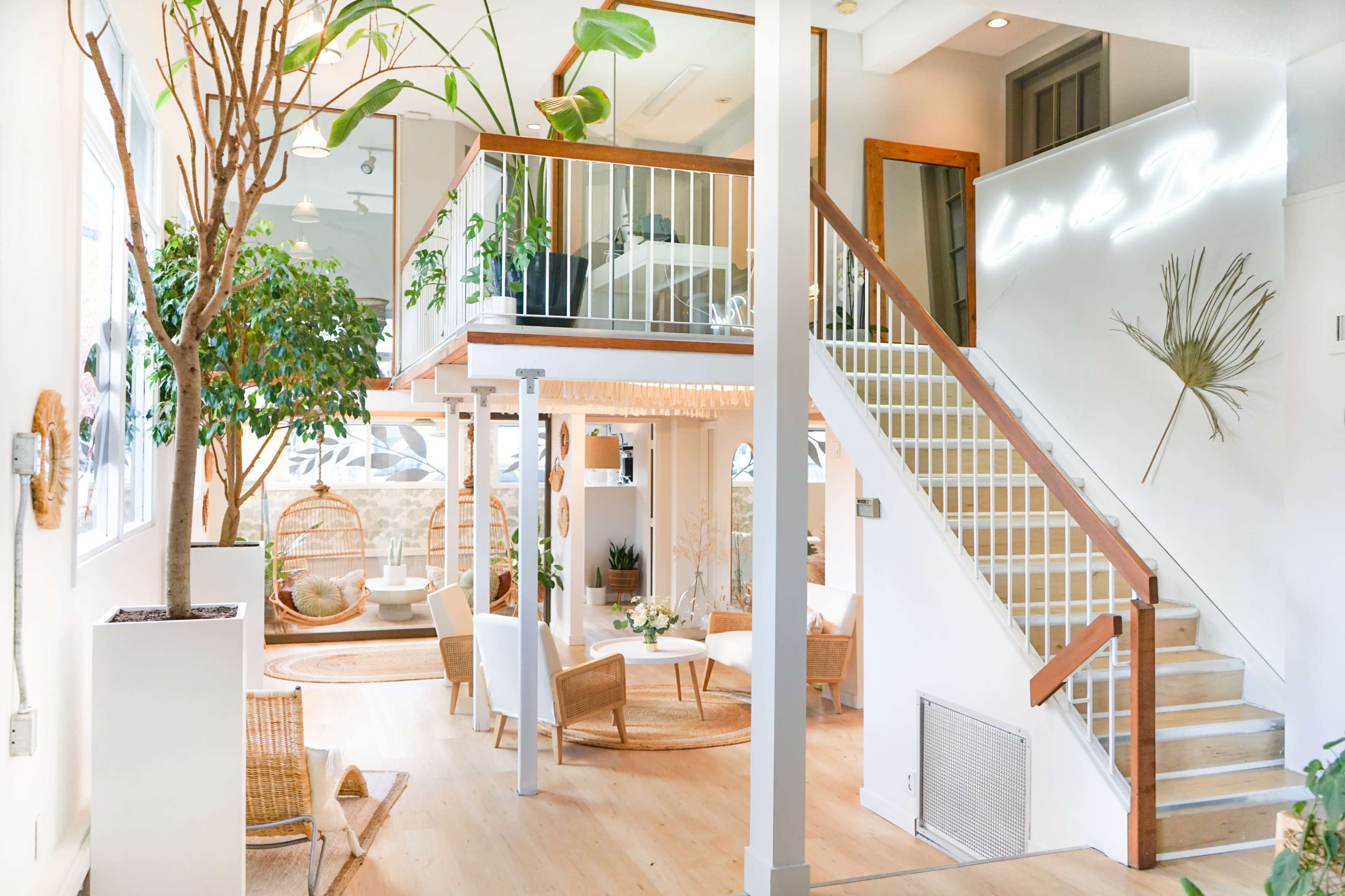 A spacious indoor area with a staircase leading to a second level, featuring plants, seating arrangements, and a well-lit ambiance.