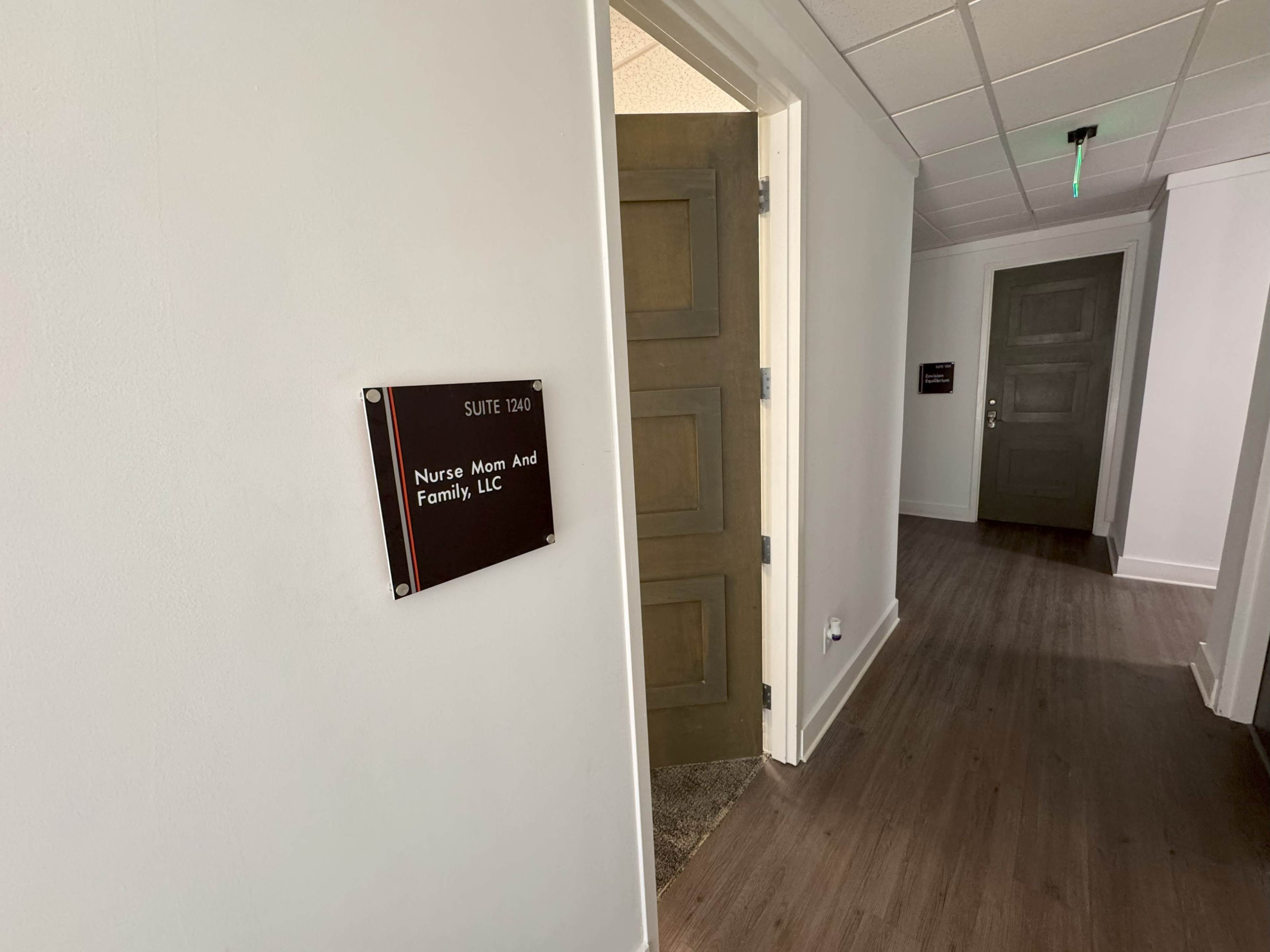 A hallway with a door leading to "Nurse Mom And Family, LLC" and a nearby suite number sign.