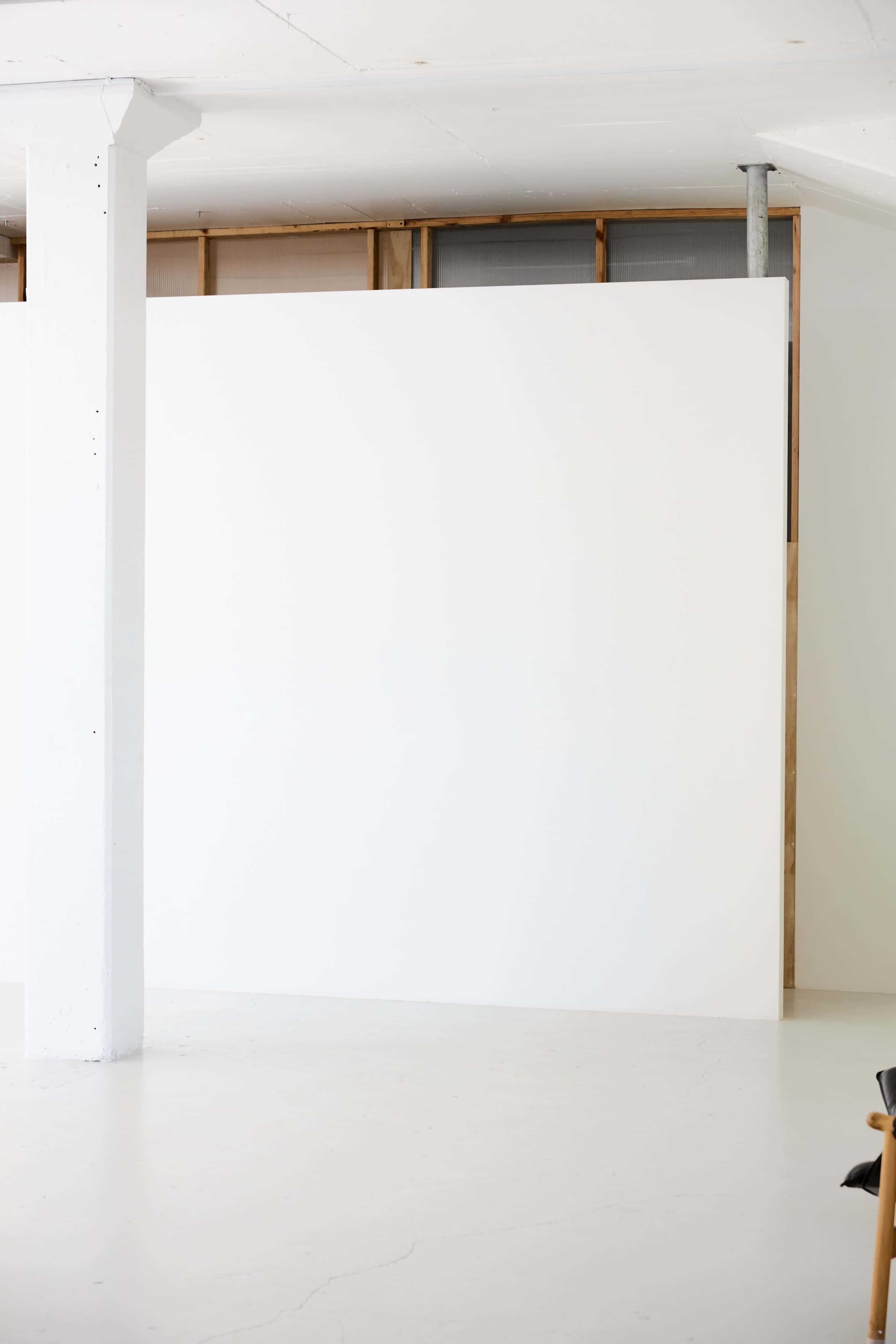 The image shows a spacious, empty room with a large white wall and a concrete pillar.