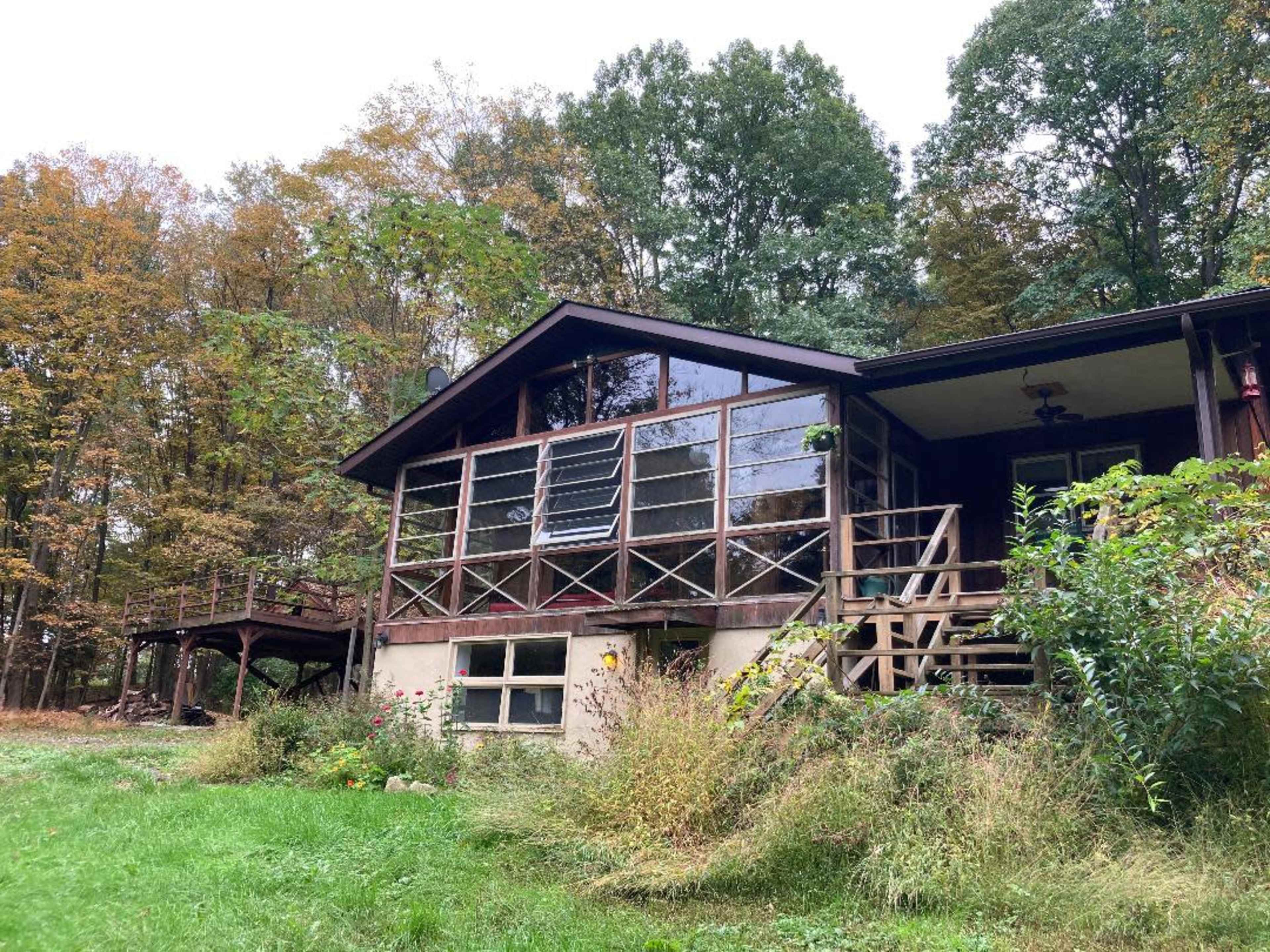 A wooden house with large glass windows is surrounded by trees and a grassy area.
