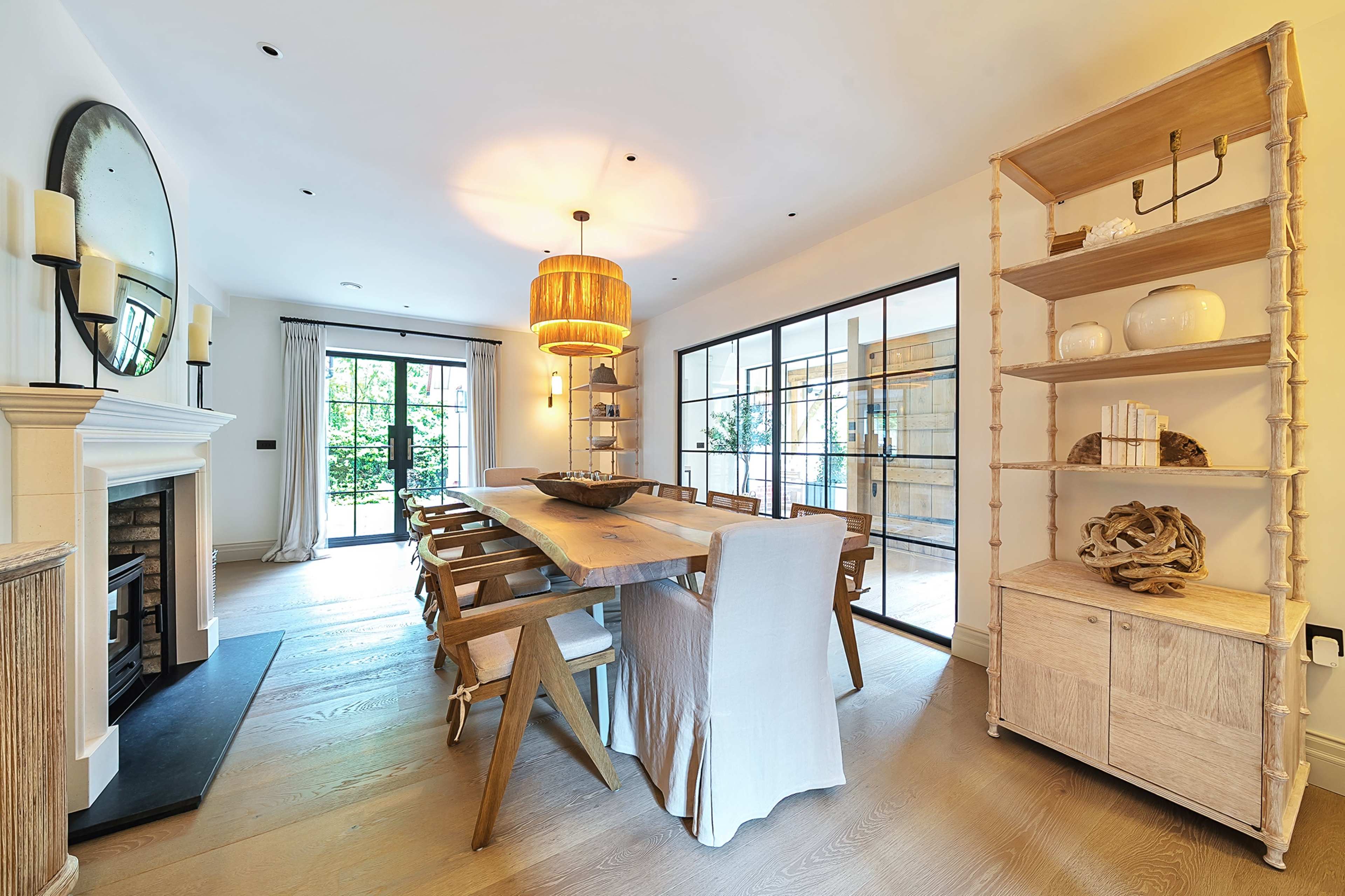 The image shows a bright dining room featuring a long wooden table, a round light fixture, and large glass doors leading to an outdoor space.